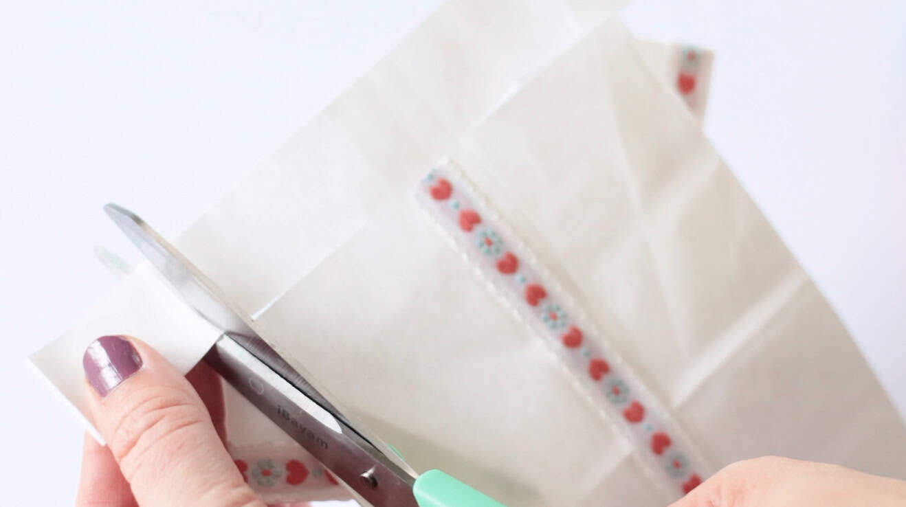 Scissors trimming the end of the white paper bag.