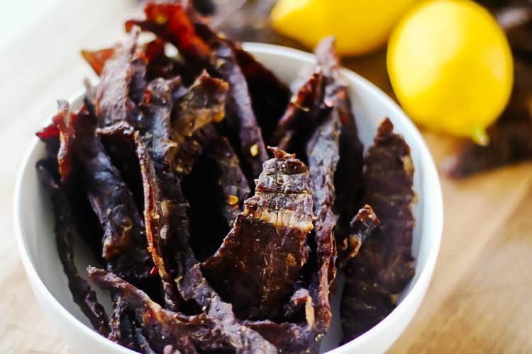 Lemon jerky strips in a white bowl with two lemons next to it.
