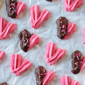 Cookie sheet of heart shaped danish cookies with some dipped in chocolate.