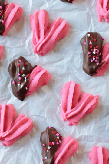 Cookie sheet of heart shaped danish cookies with some dipped in chocolate.