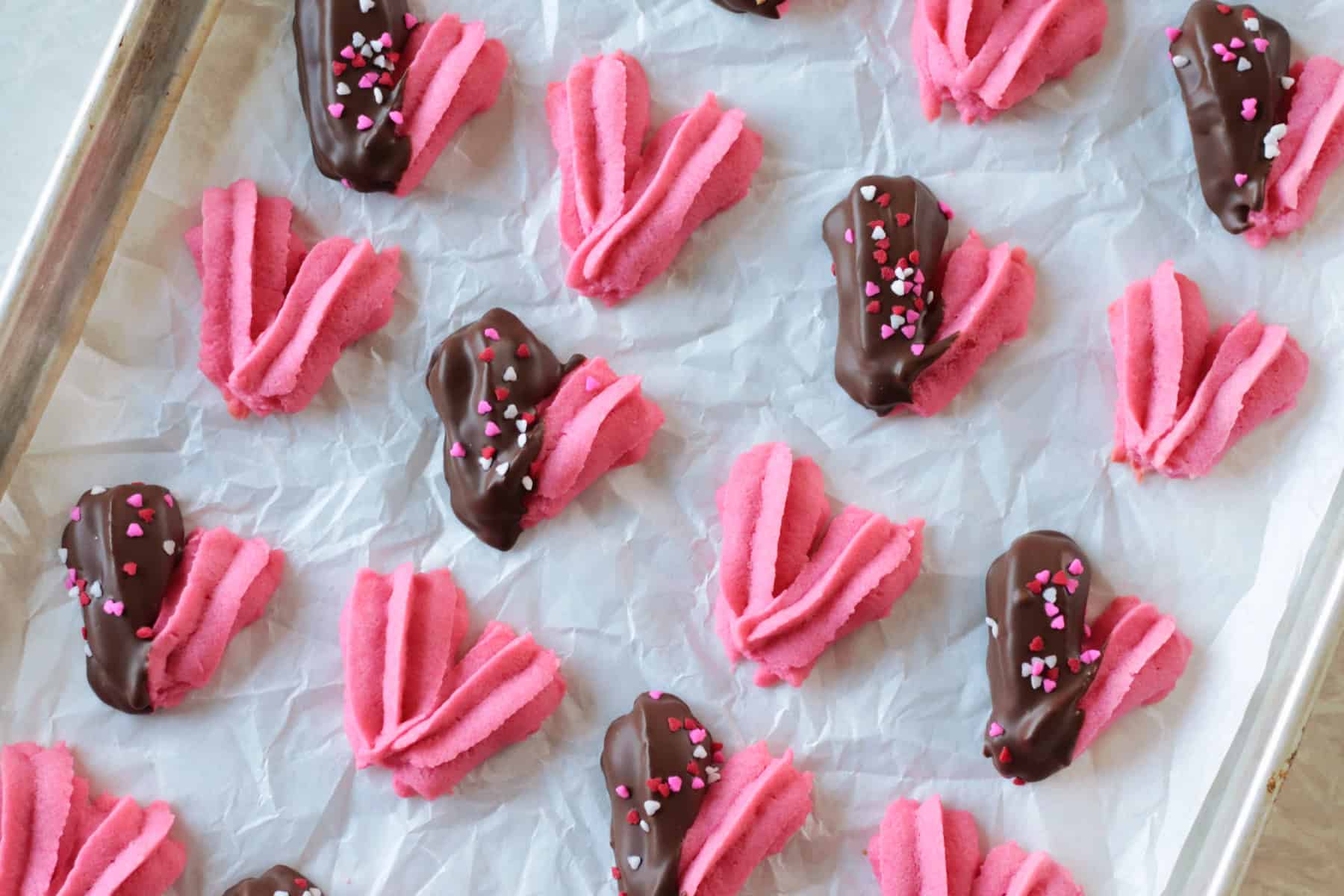 Cookie sheet of heart shaped danish cookies with some dipped in chocolate.