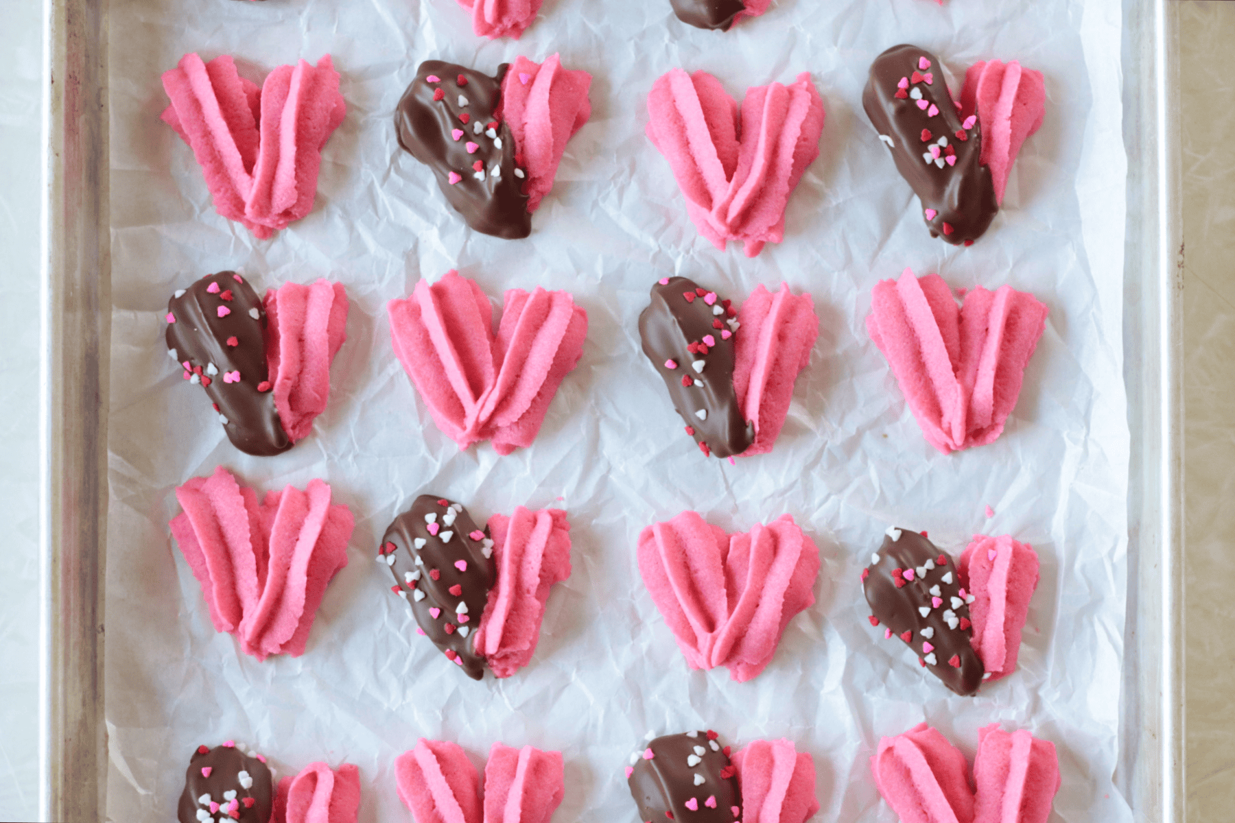 Cookie sheet of heart shaped danish cookies with some dipped in chocolate.