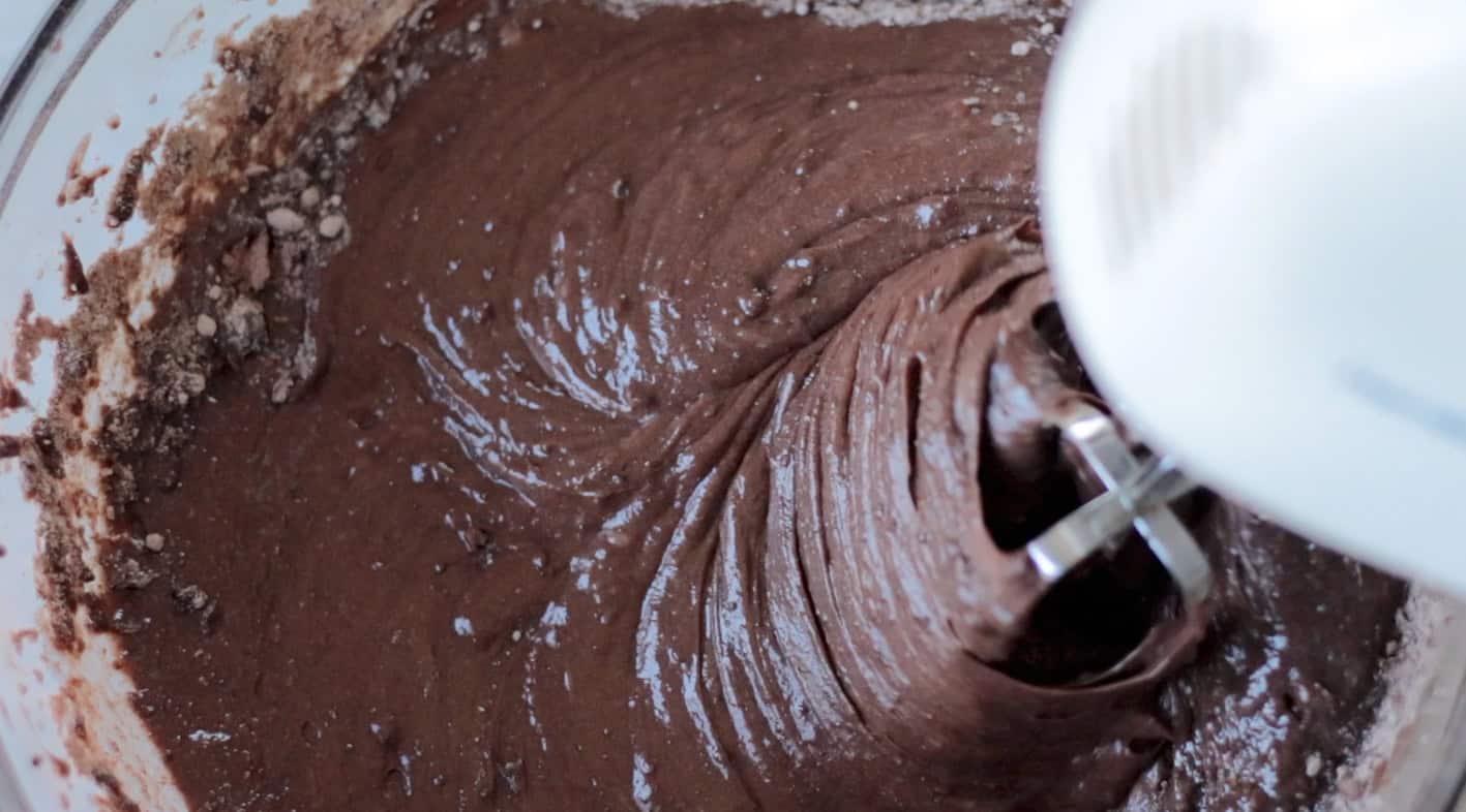 Electric beater mixing chocolate cake batter in mixing bowl.