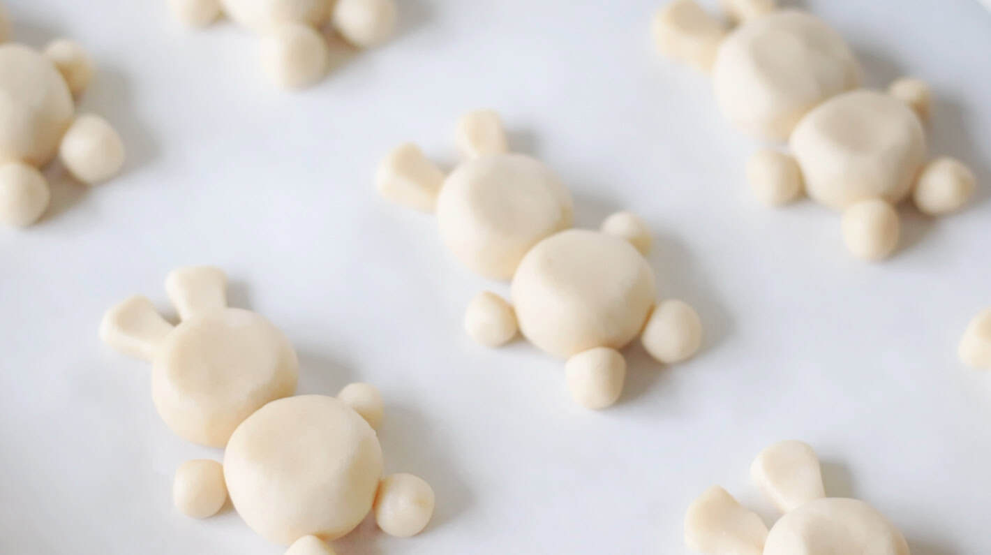Balls of cookie dough shaped as bunnies on a baking sheet.