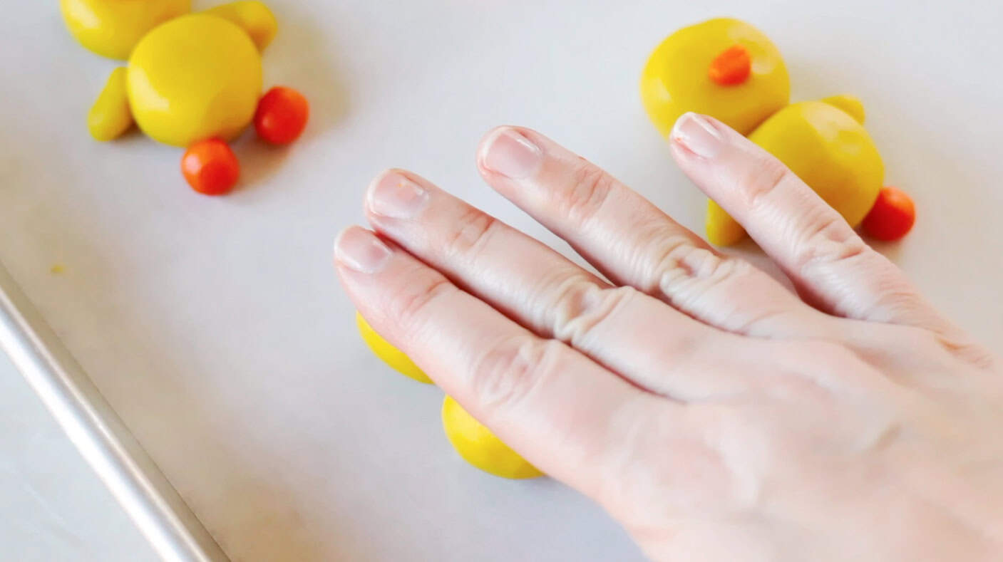 Hand pressing down on sugar cookie dough balls.