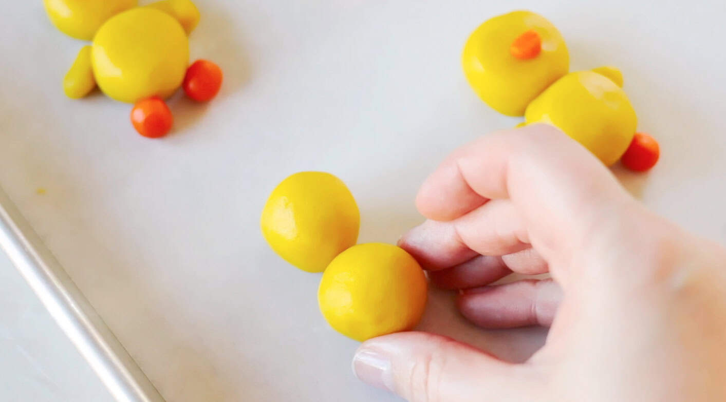 Hand positioning yellow cookie dough balls in place.