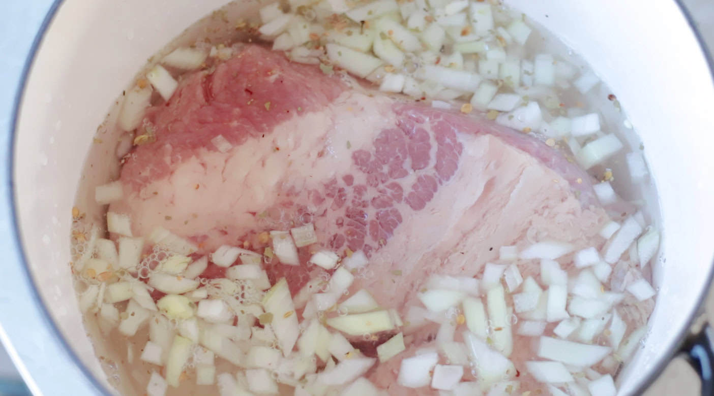 Onions and corned beef brisket with water covering in Dutch oven.