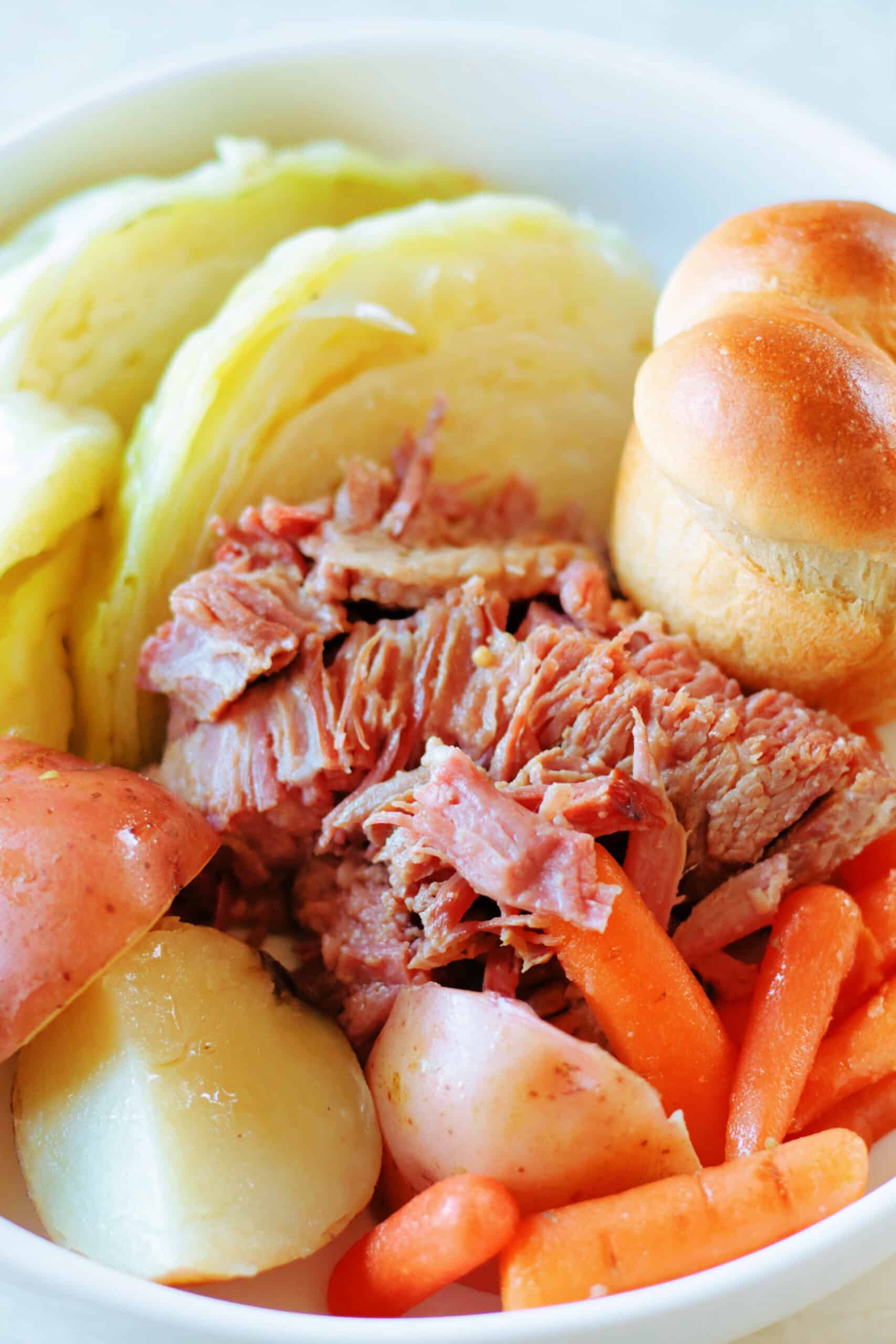Corned beef, cabbage, carrots, potatoes and roll in serving dish.