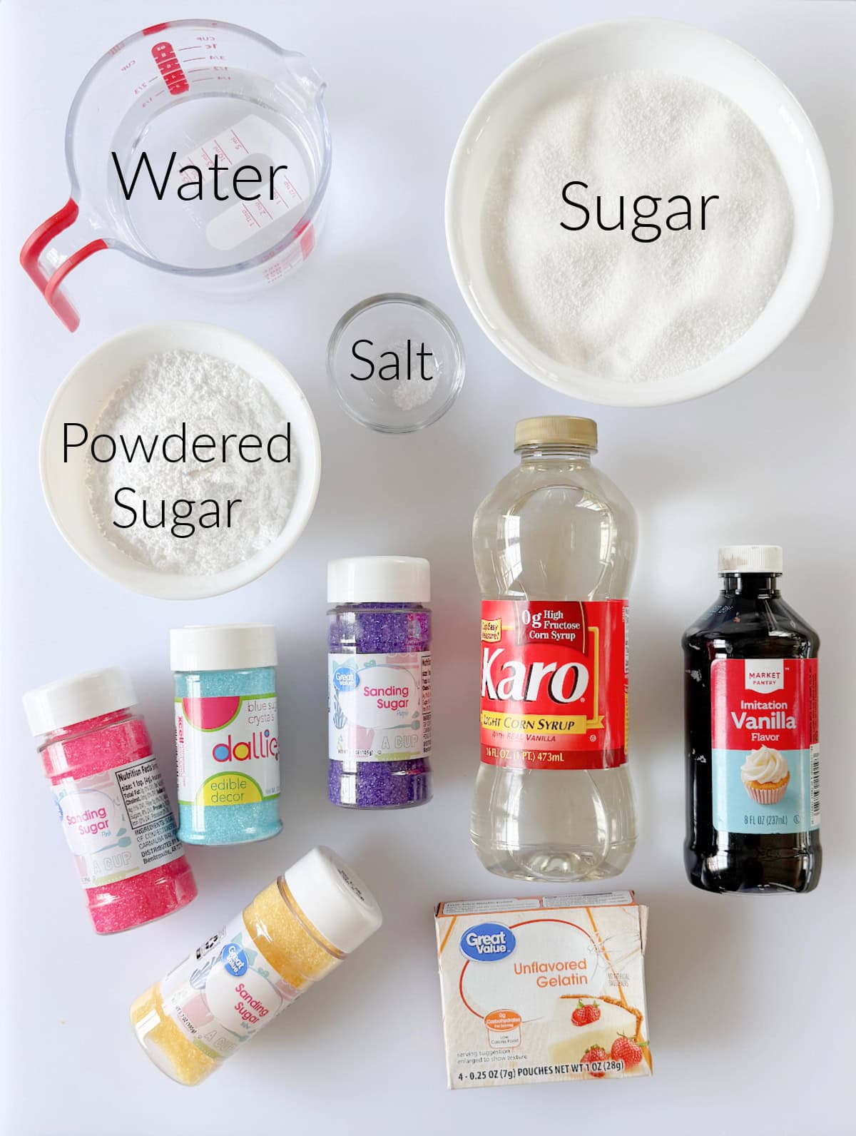 Bowls of sugar, powdered sugar, salt and water with bottles of vanilla and corn syrup. Box of unflavored gelatin and bottles of sprinkles.