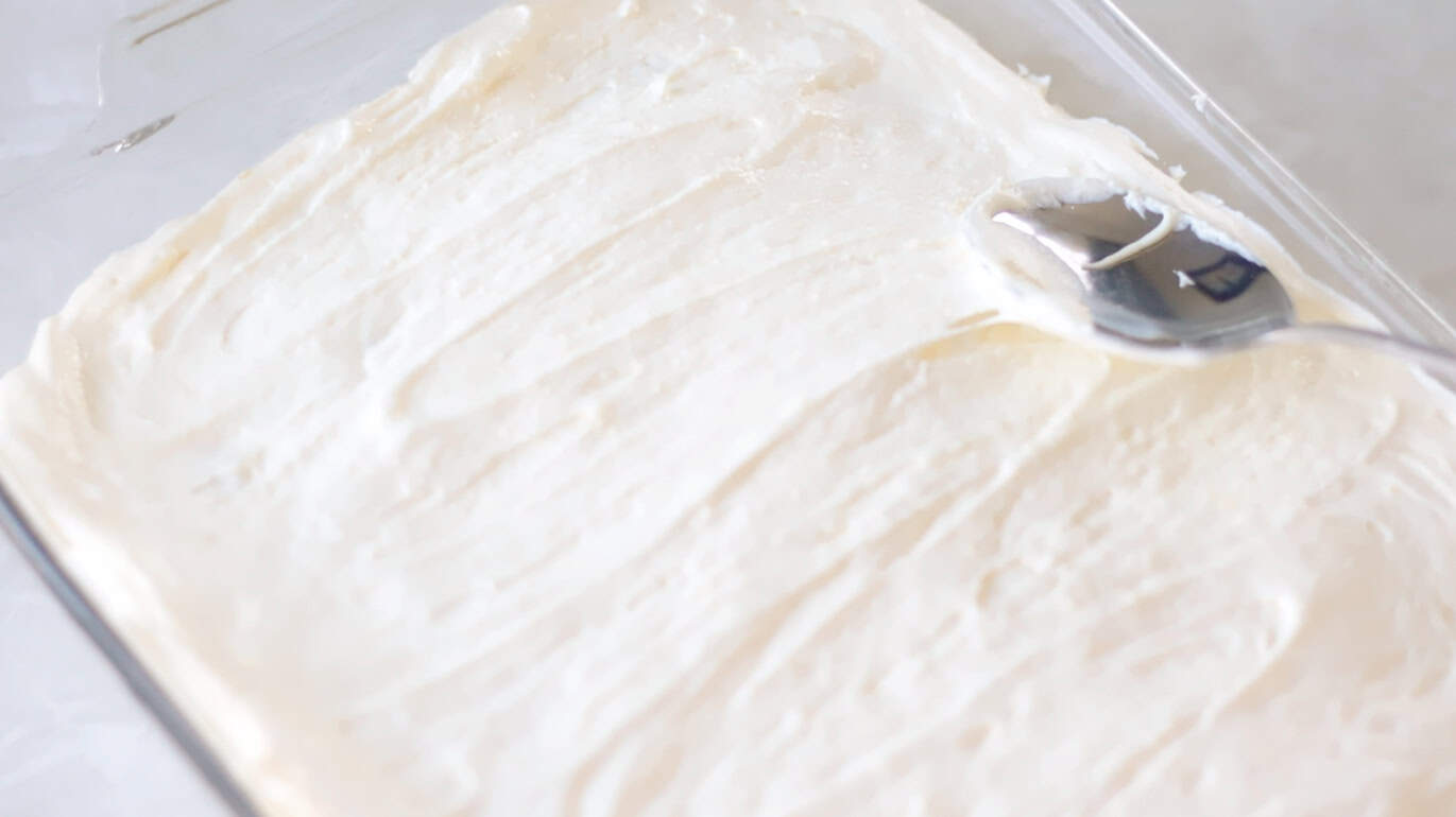 Spoon spreading vanilla pudding over sliced bananas.