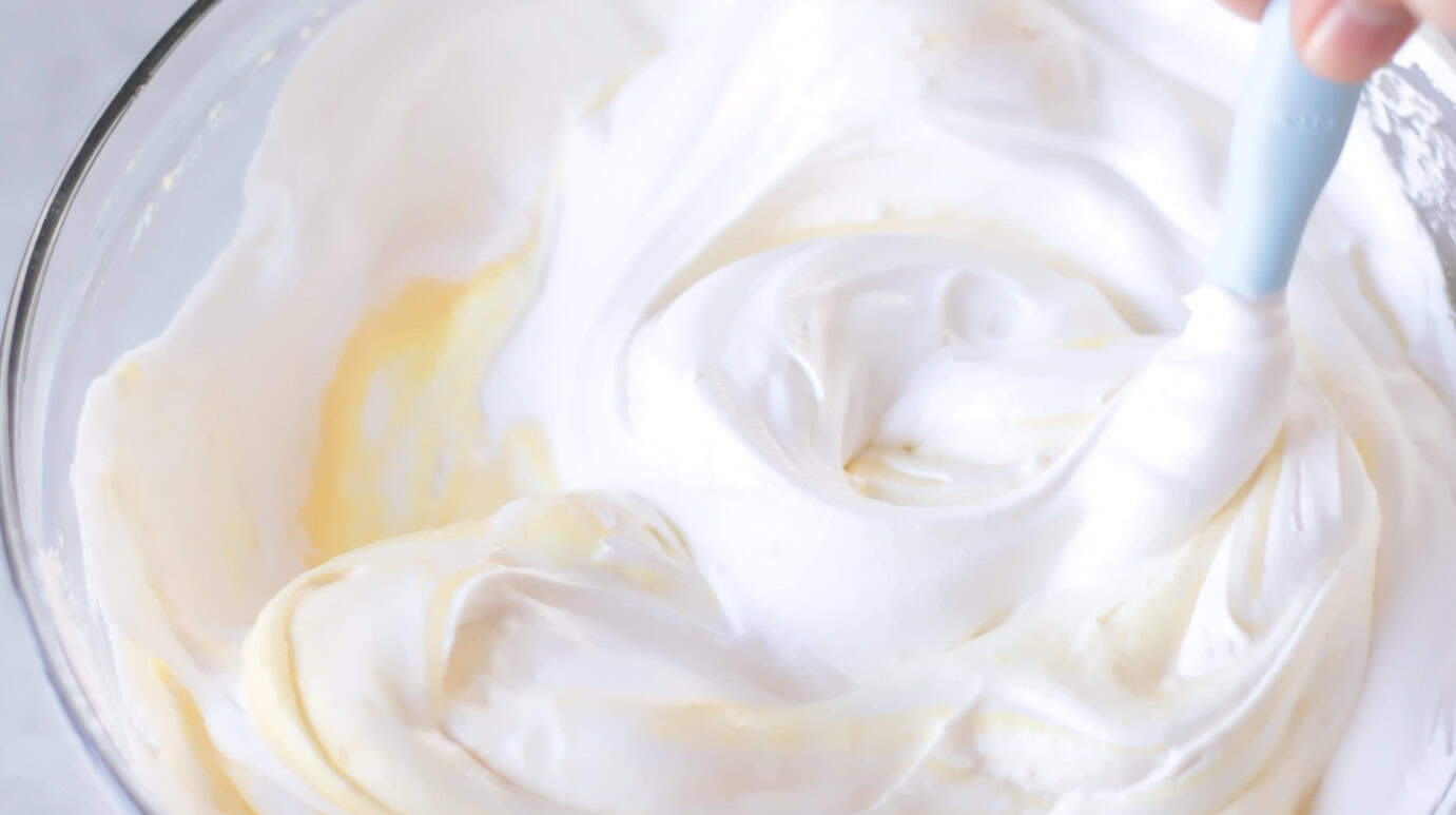 Glass mixing bowl with whipped cream and vanilla pudding.