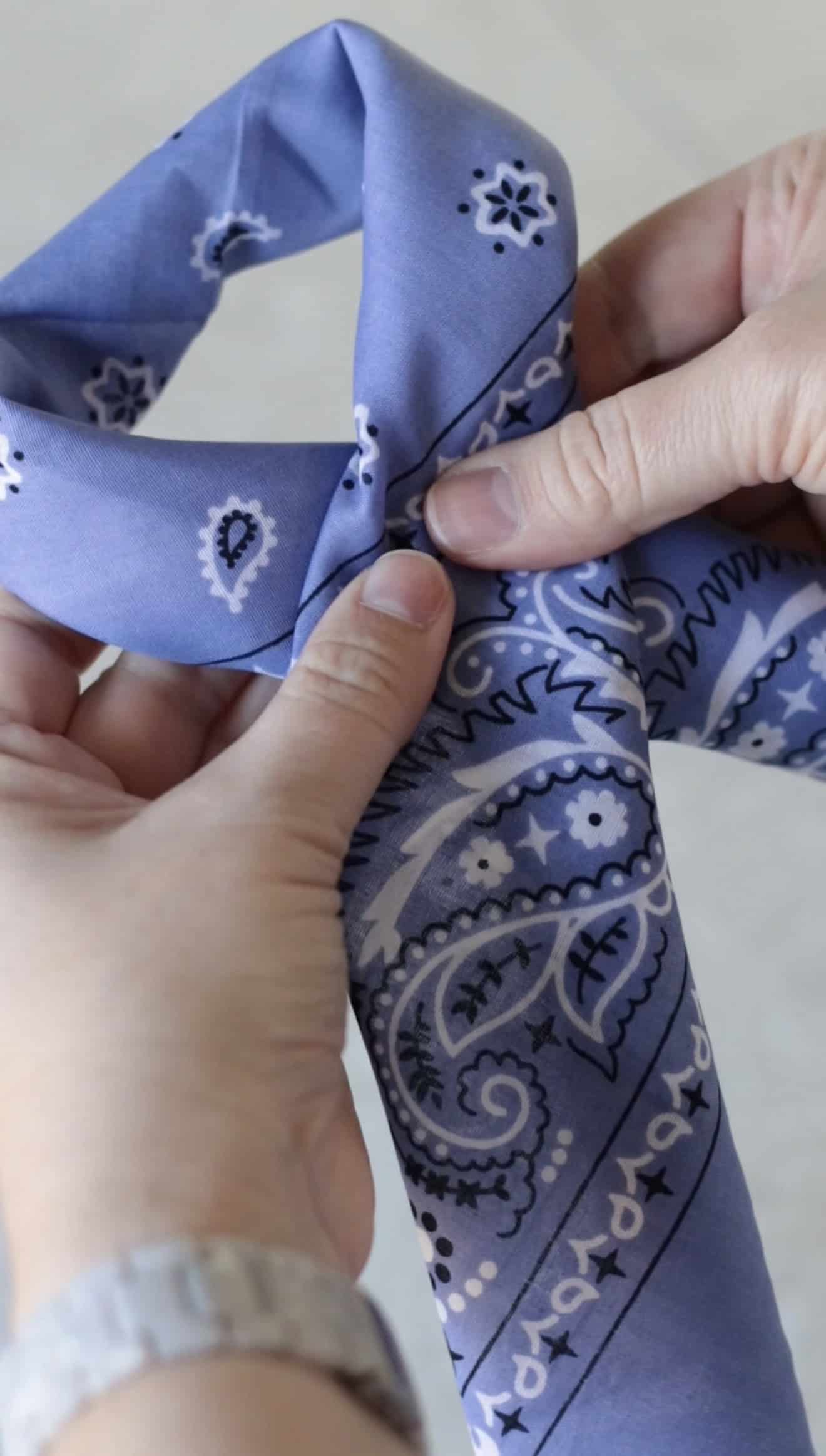 Hand holding purple bandana rolled up and folded over.