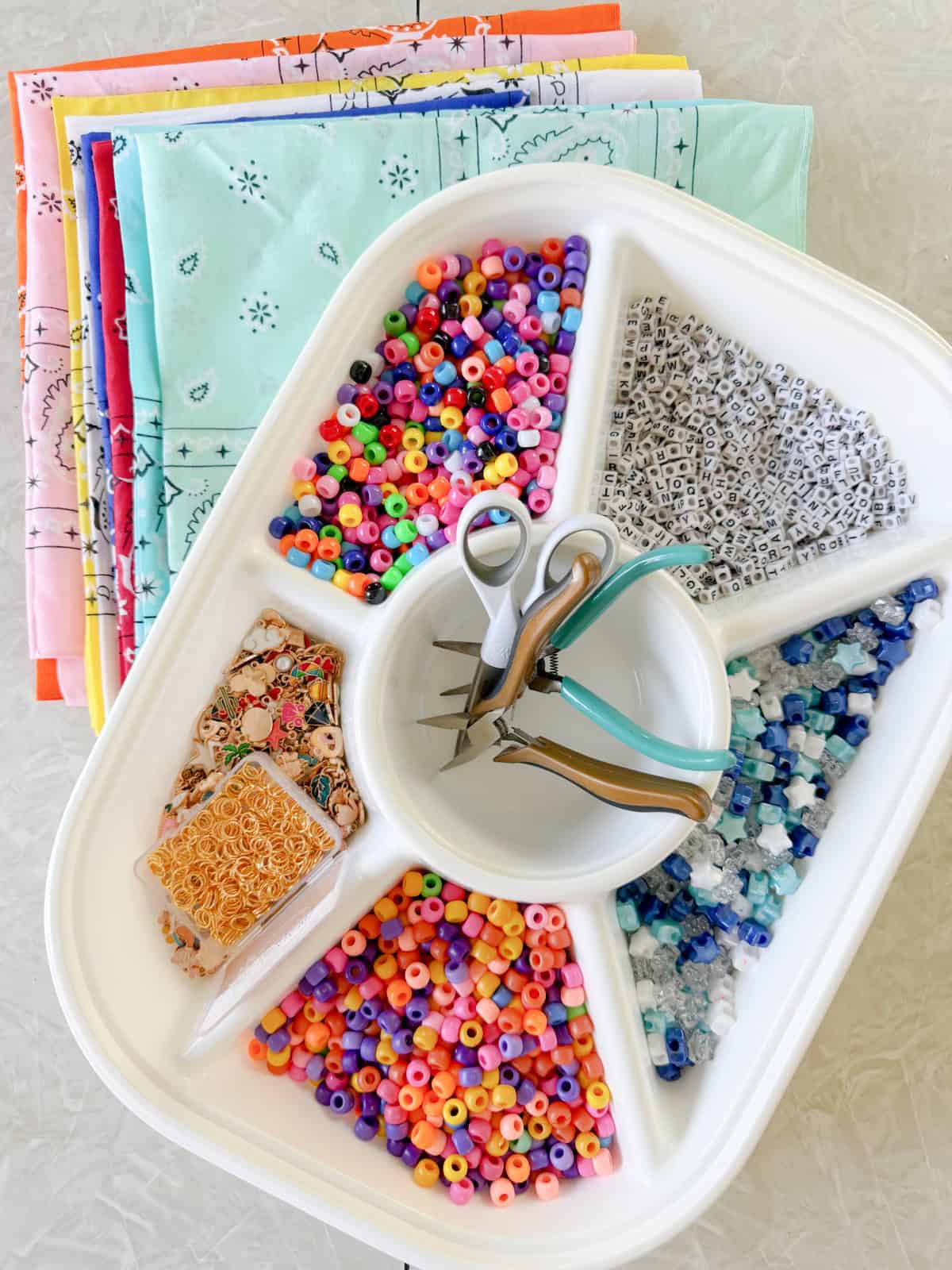 Divided tray with beads, scissors and stack of folded bandanas.