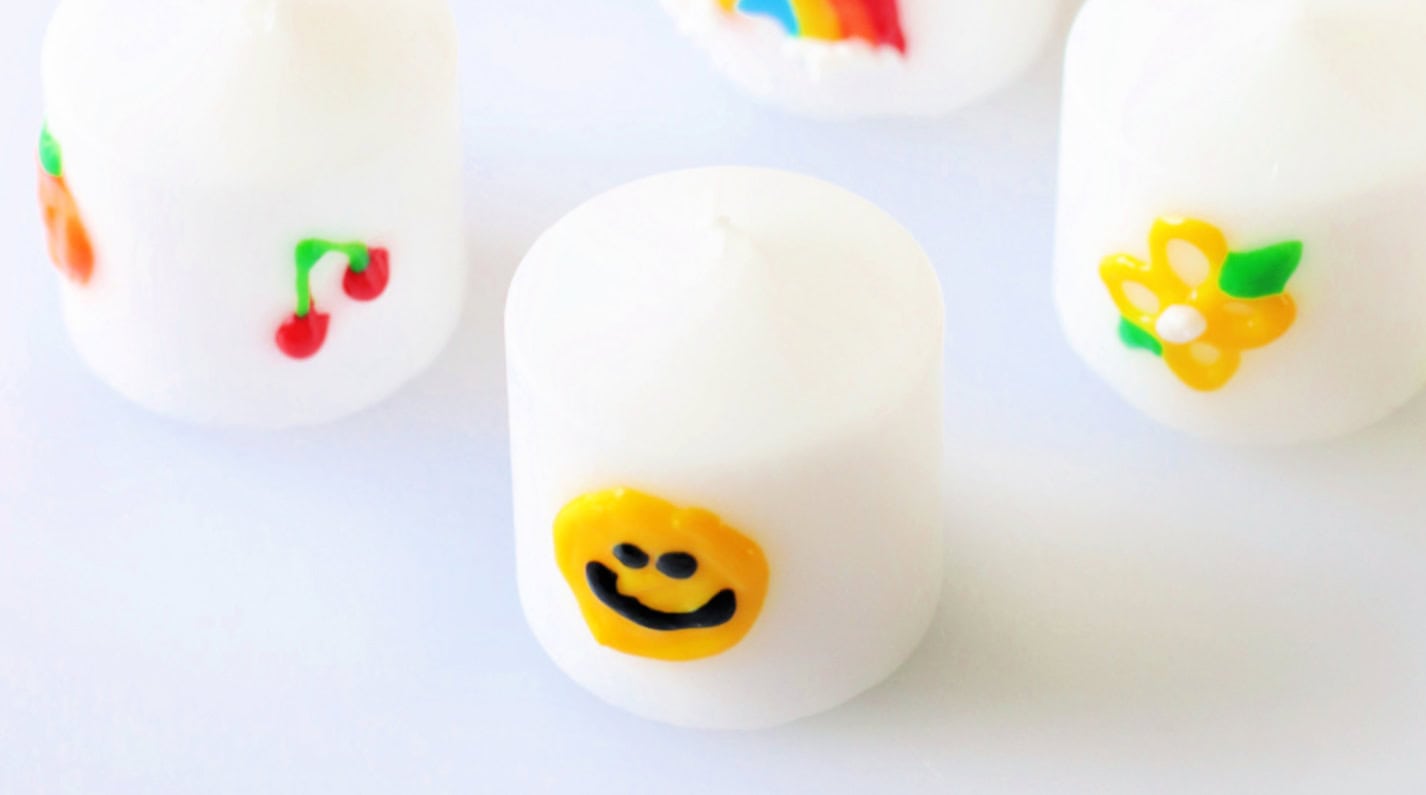 White candle votive decorated with yellow smiley face.