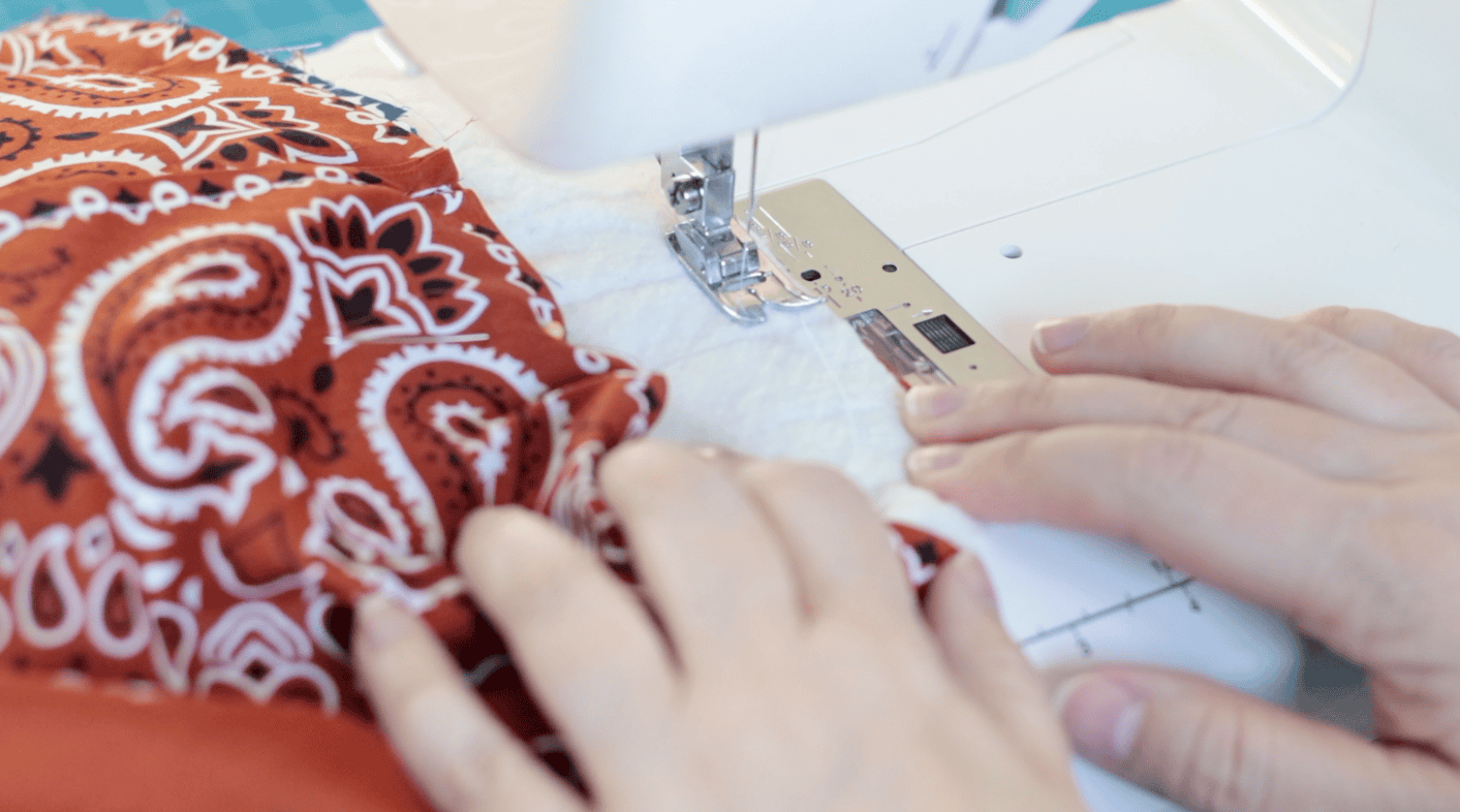 Sewing machine stitching the top of a bag.