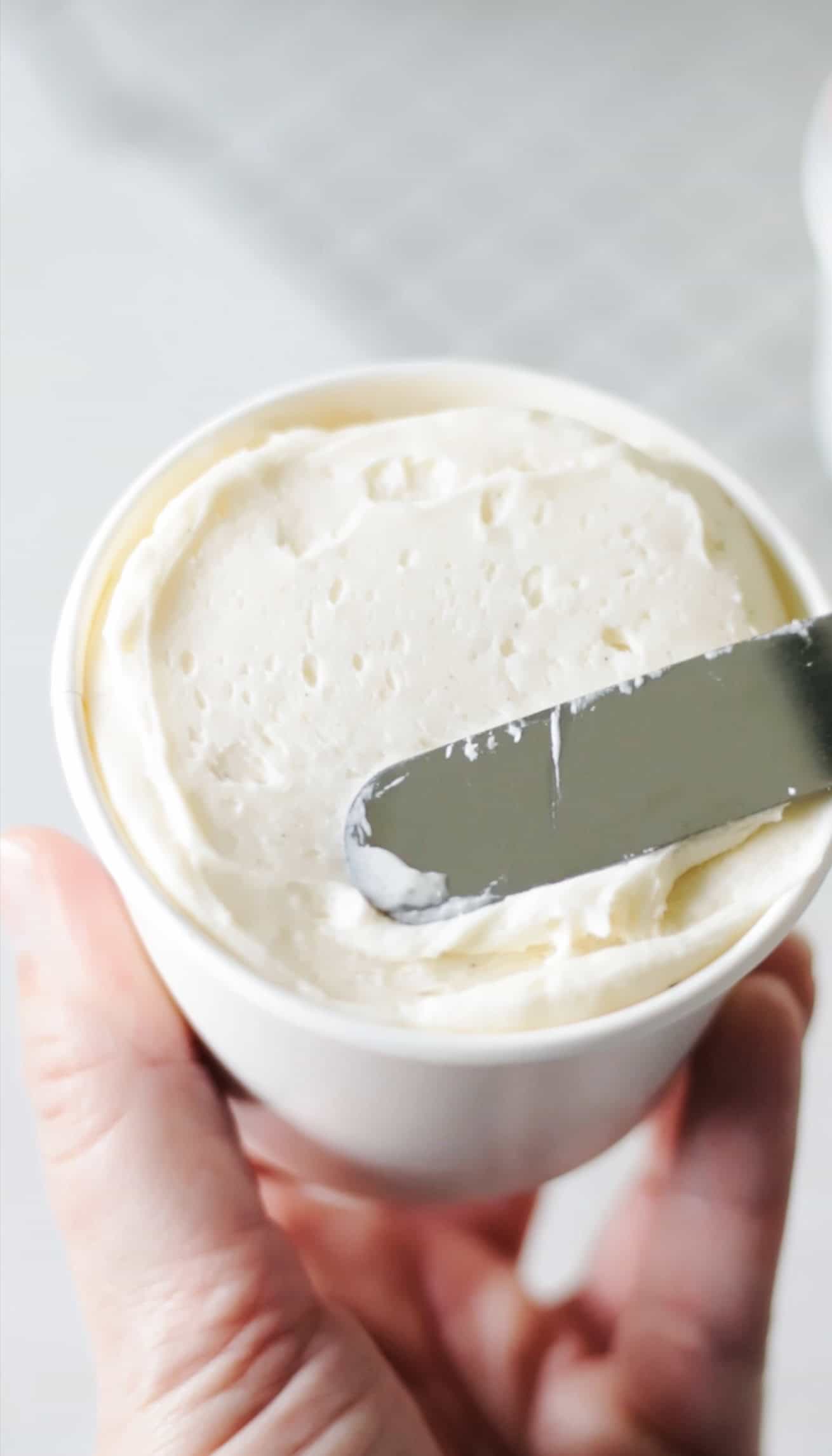 Spatula spreading frosting over cupcake in a cup.