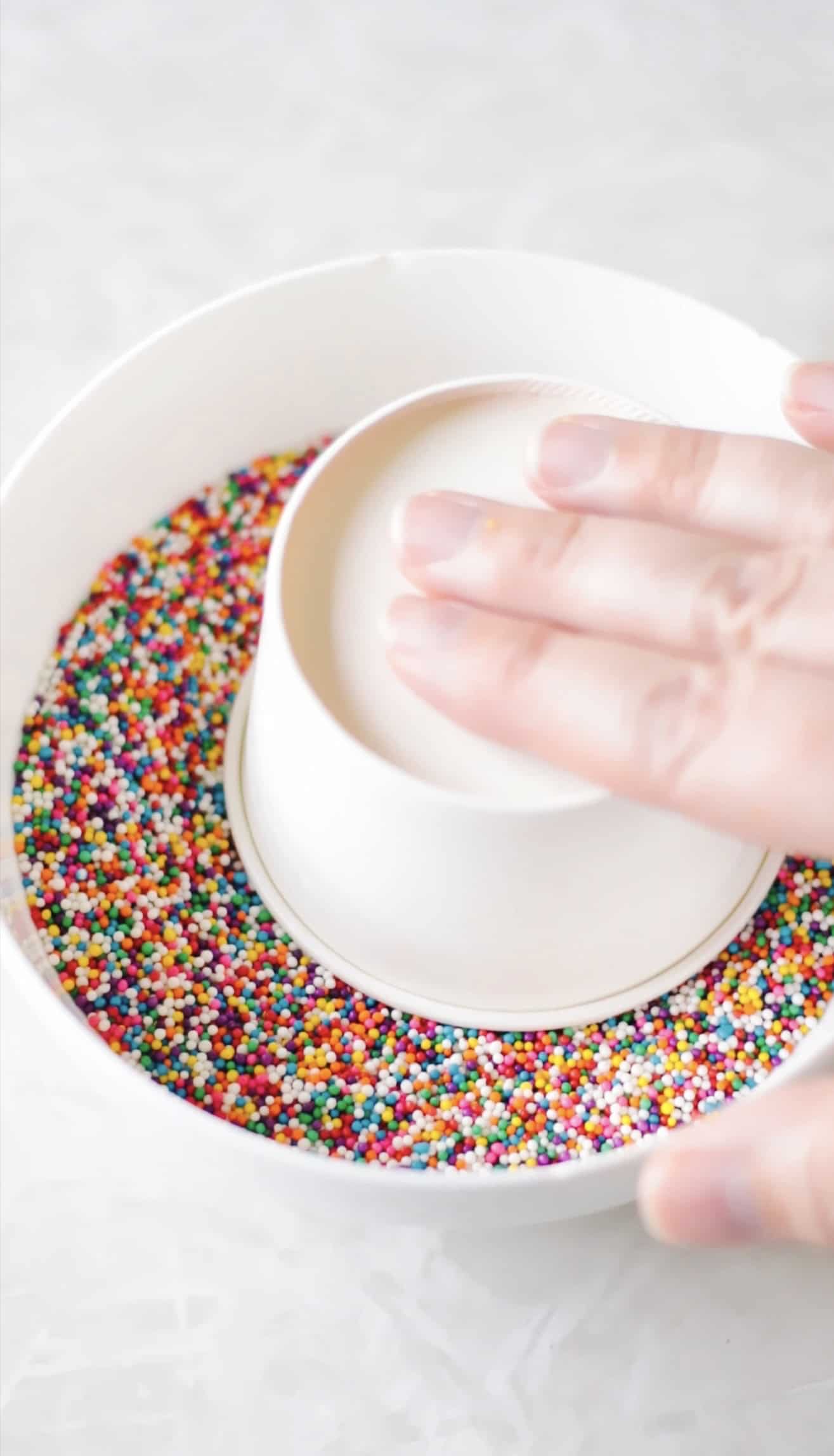 Hand-pressing dot cake into a bowl of sprinkles.