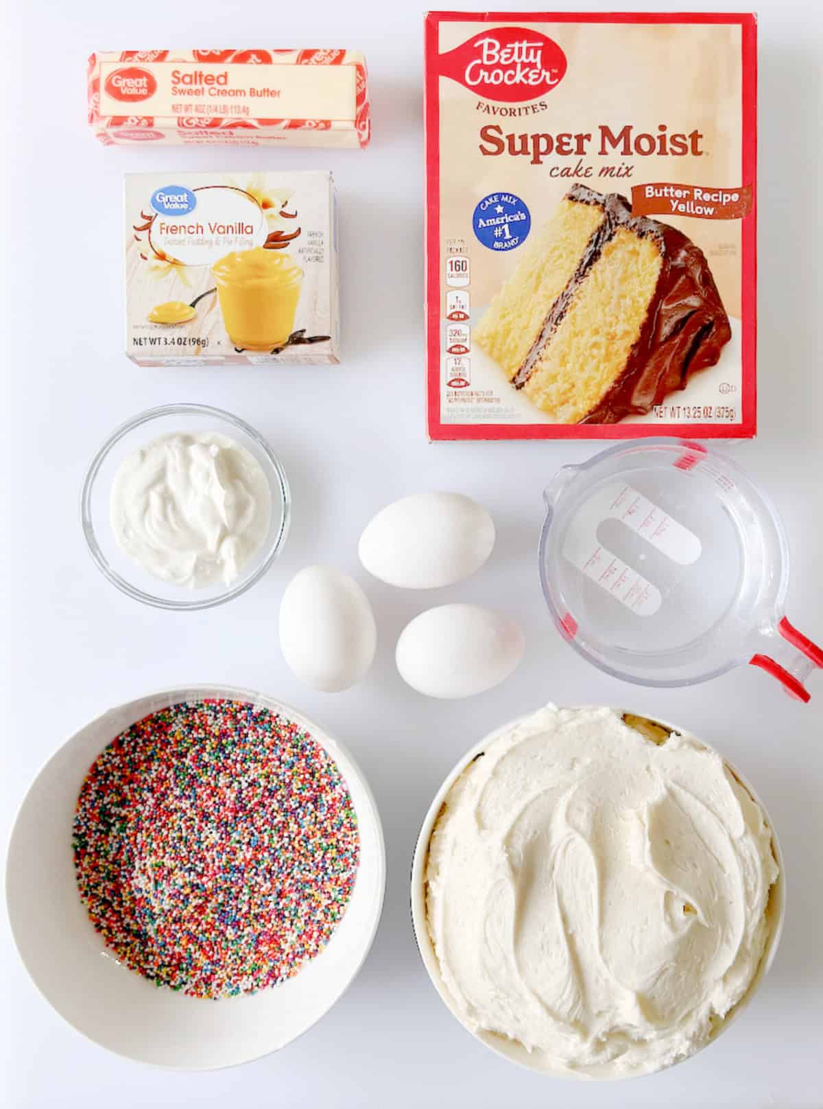 Box of cake mix, box of vanilla pudding mix, bowl of sour cream, cup of water, 3 eggs, bowl of frosting and bowl of rainbow sprinkles.
