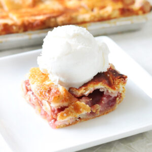 Slice of strawberry rhubarb pie on plate with scoop of vanilla ice cream.