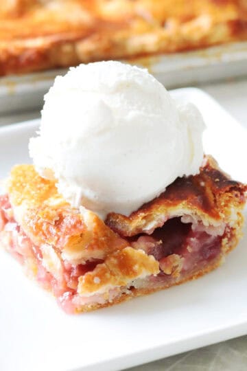 Slice of strawberry rhubarb pie on plate with scoop of vanilla ice cream.