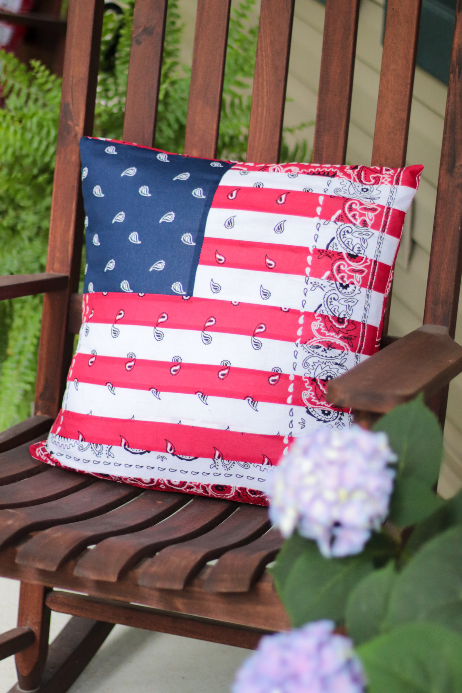 Bandana pillow on rocking chair next to pot of flowers.