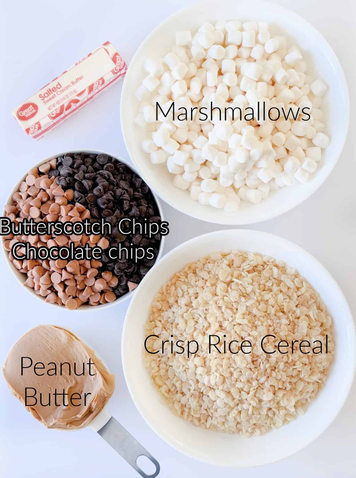 Bowls of marshmallows, cereal, chocolate chips and butterscotch chips, stick of butter and cup of peanut butter