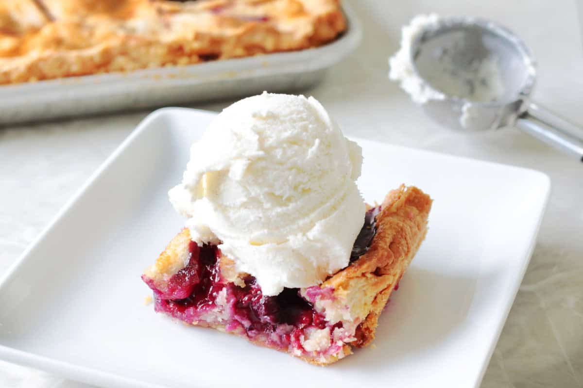 Slice of mixed berry slab pie with ice cream on plate.