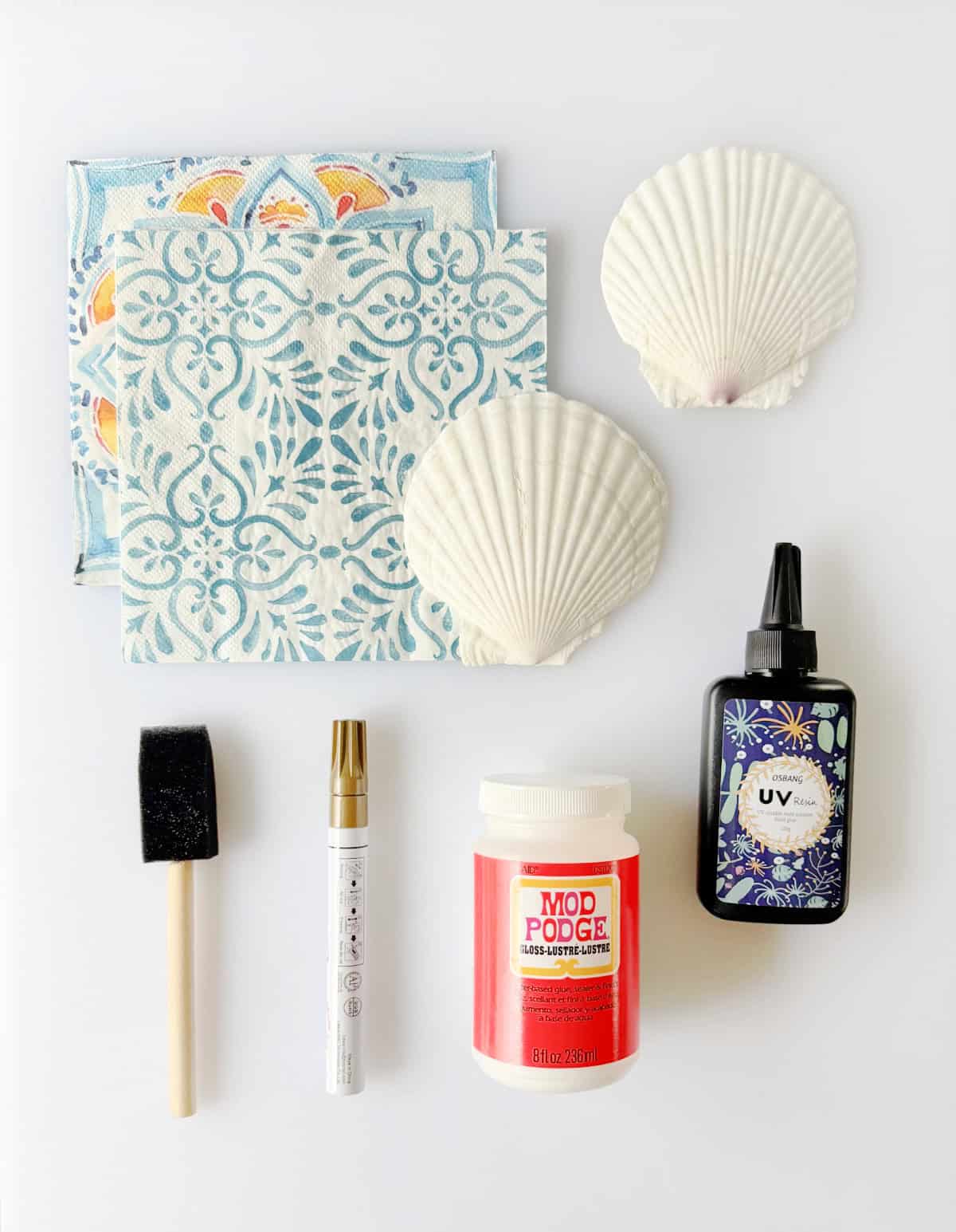 Two decorated napkins, two scallop shells, sponge brush, gold paint pen, bottle of mod podge and bottle of UV resin.