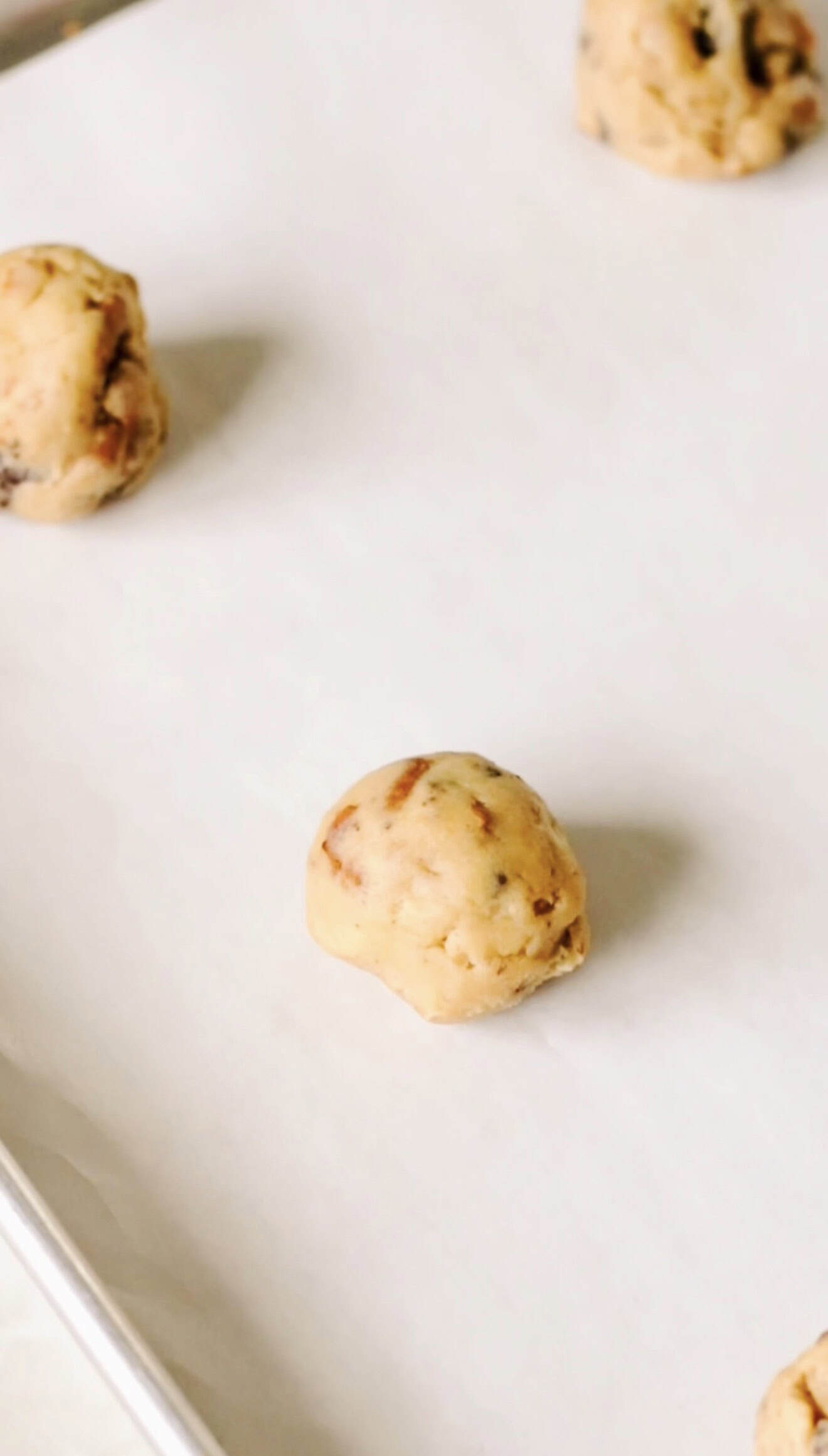 Cookie dough balls on parchment-lined baking sheet.