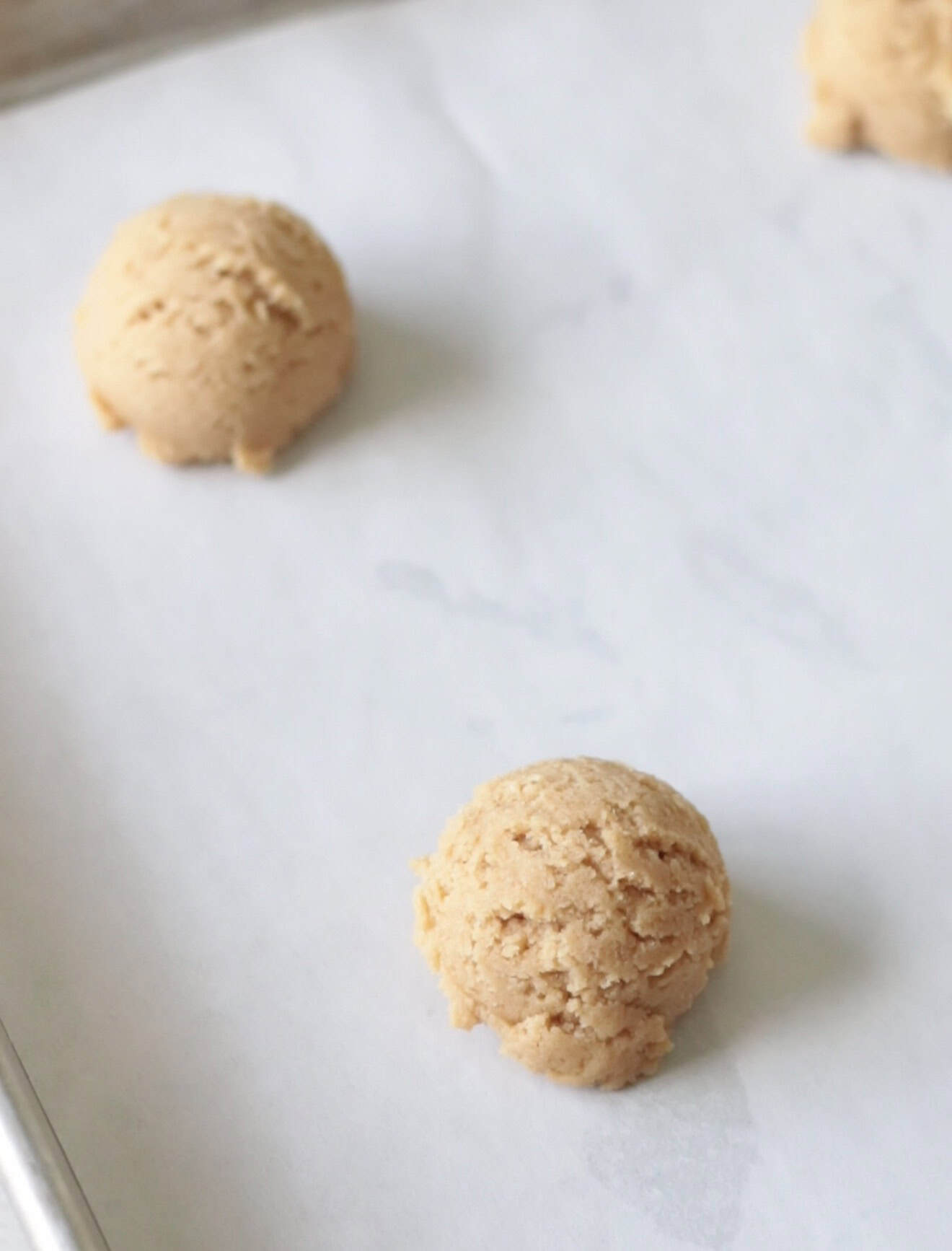 Balls of cookie dough on a parchment-paper lined baking sheet.