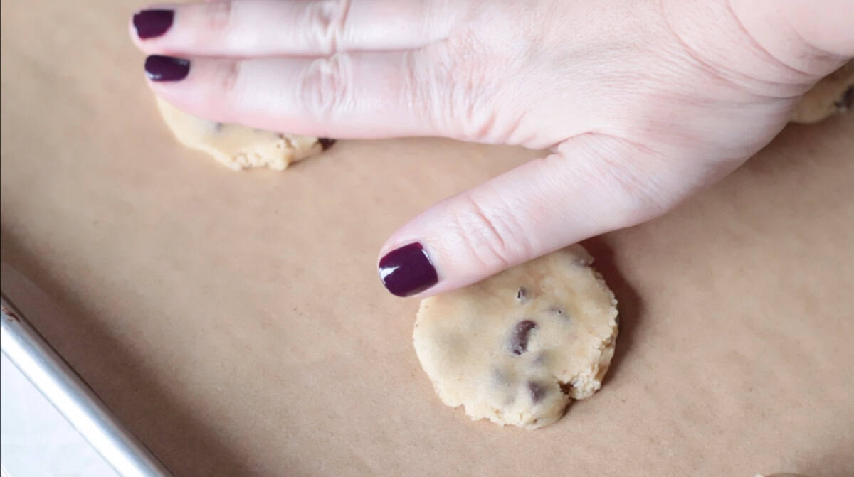 Hand placing chocolate chip cookie on baking sheet for Tate's Bake Shop recipe.