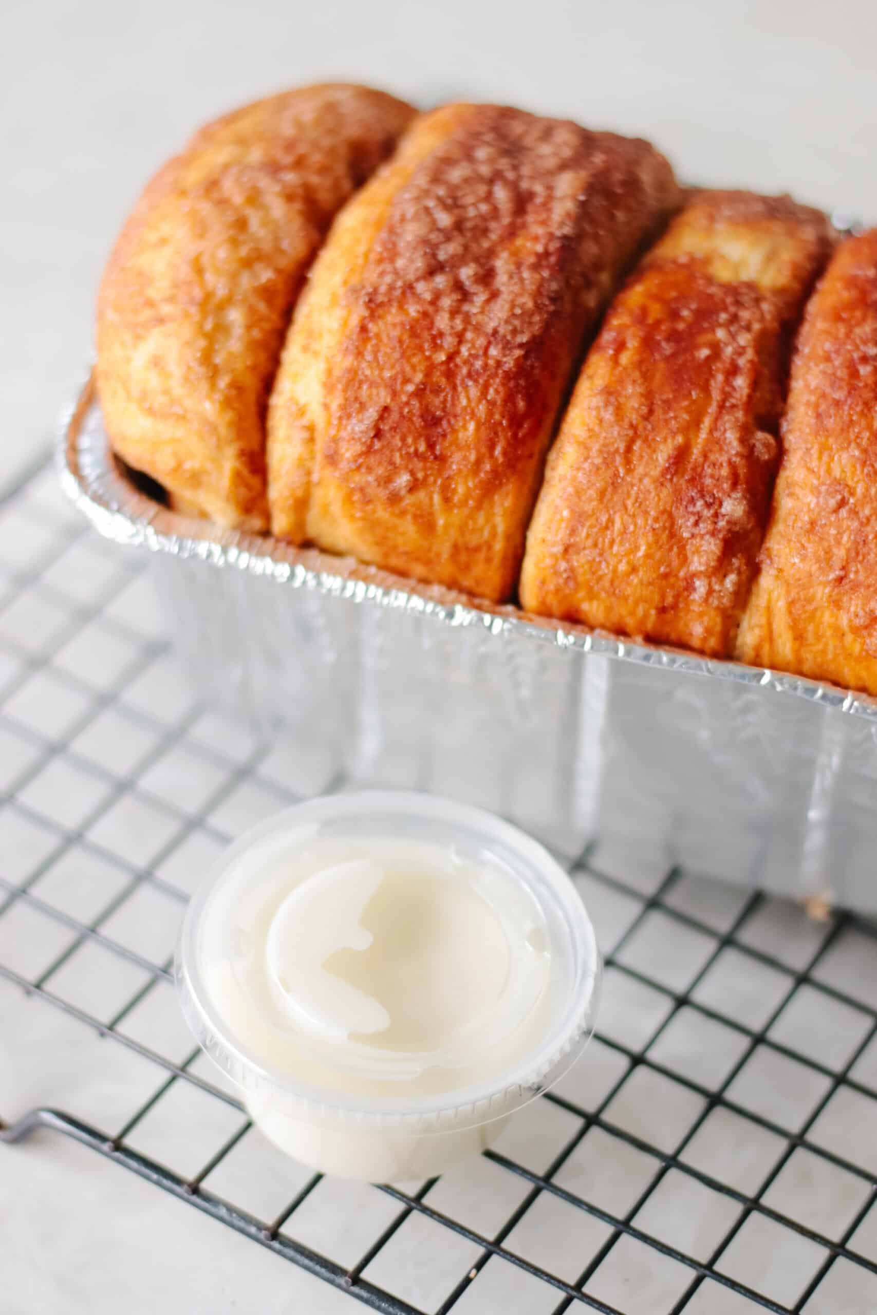 Loaf of cinnamon bread on cooling rack and small container of icing.