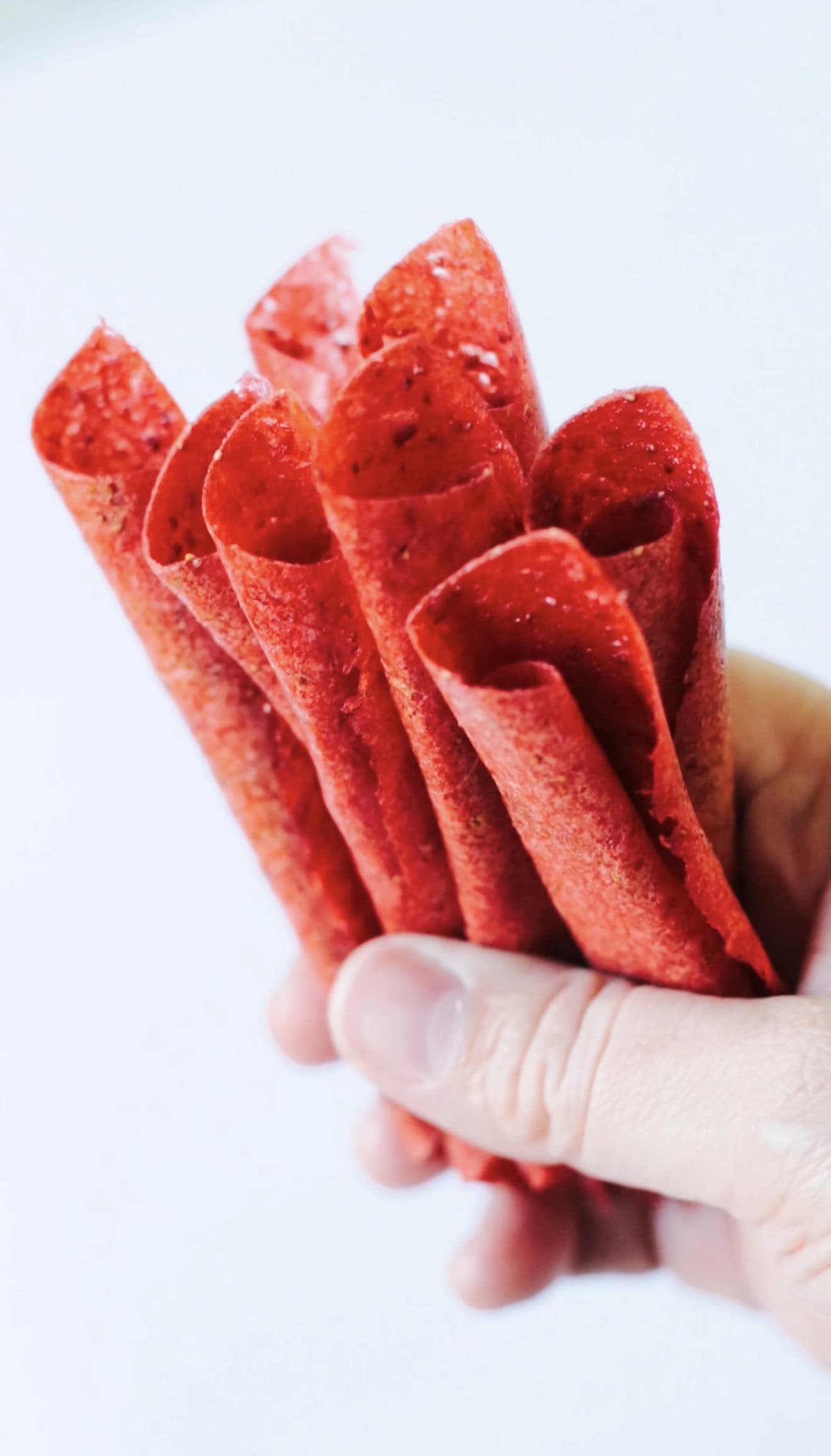 Hand holding rolls of strawberry fruit leather.