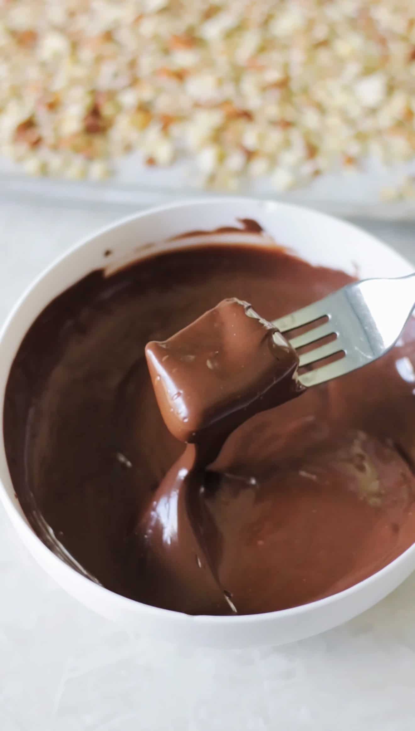 Toffee dipped in melted chocolate with fork.
