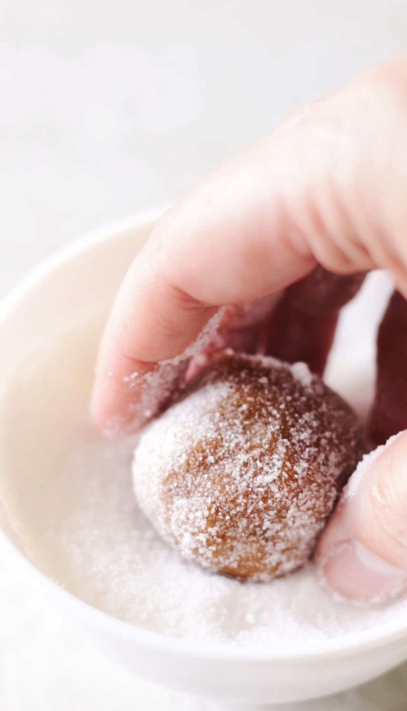 Hand rolling ball of cookie dough into granulated sugar.