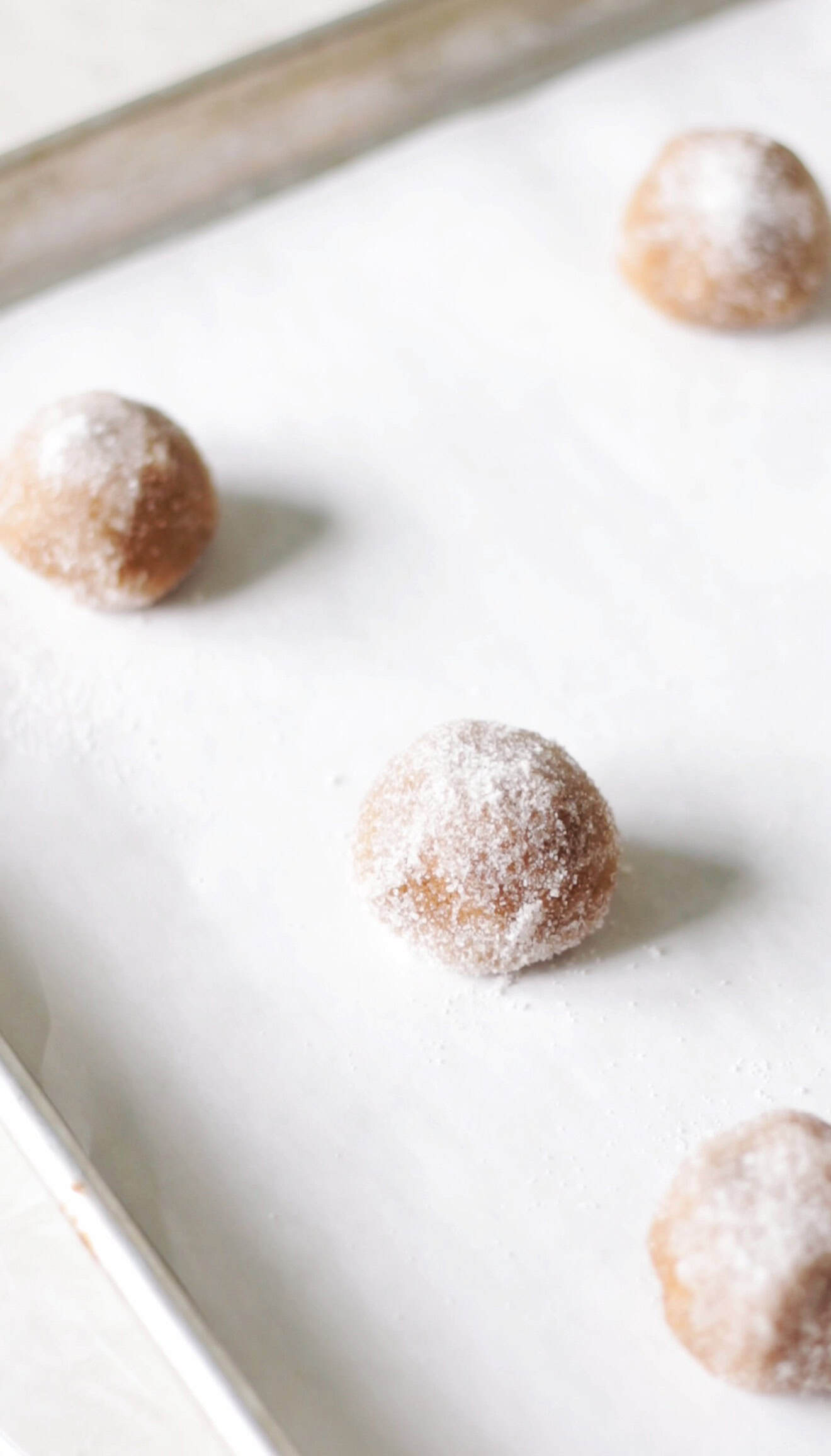 Balls of molasses cookie dough rolled in sugar and placed on baking sheet.