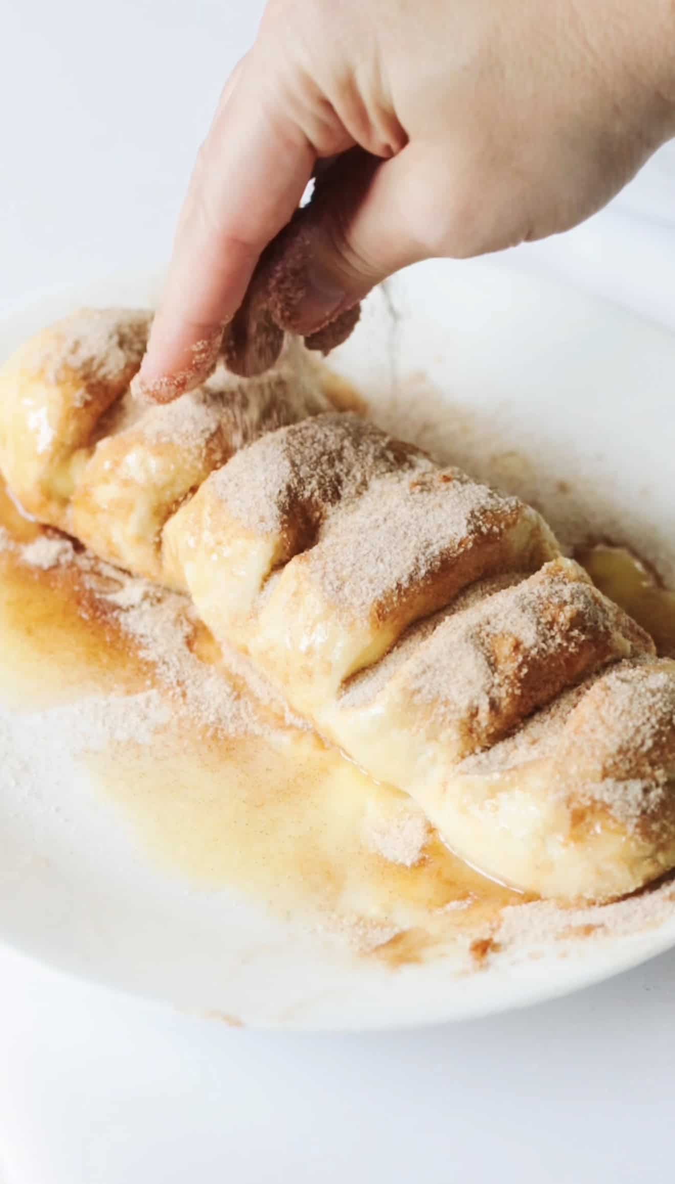 Hand sprinkling cinnamon and sugar all over loaf of bread dough.