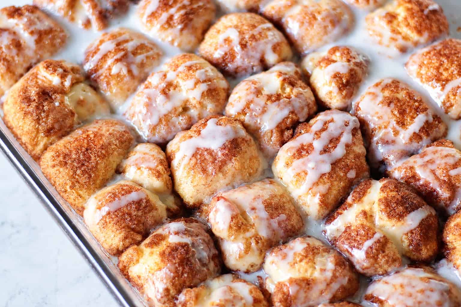 Baking dish of cinnamon roll bites drizzled in glaze.