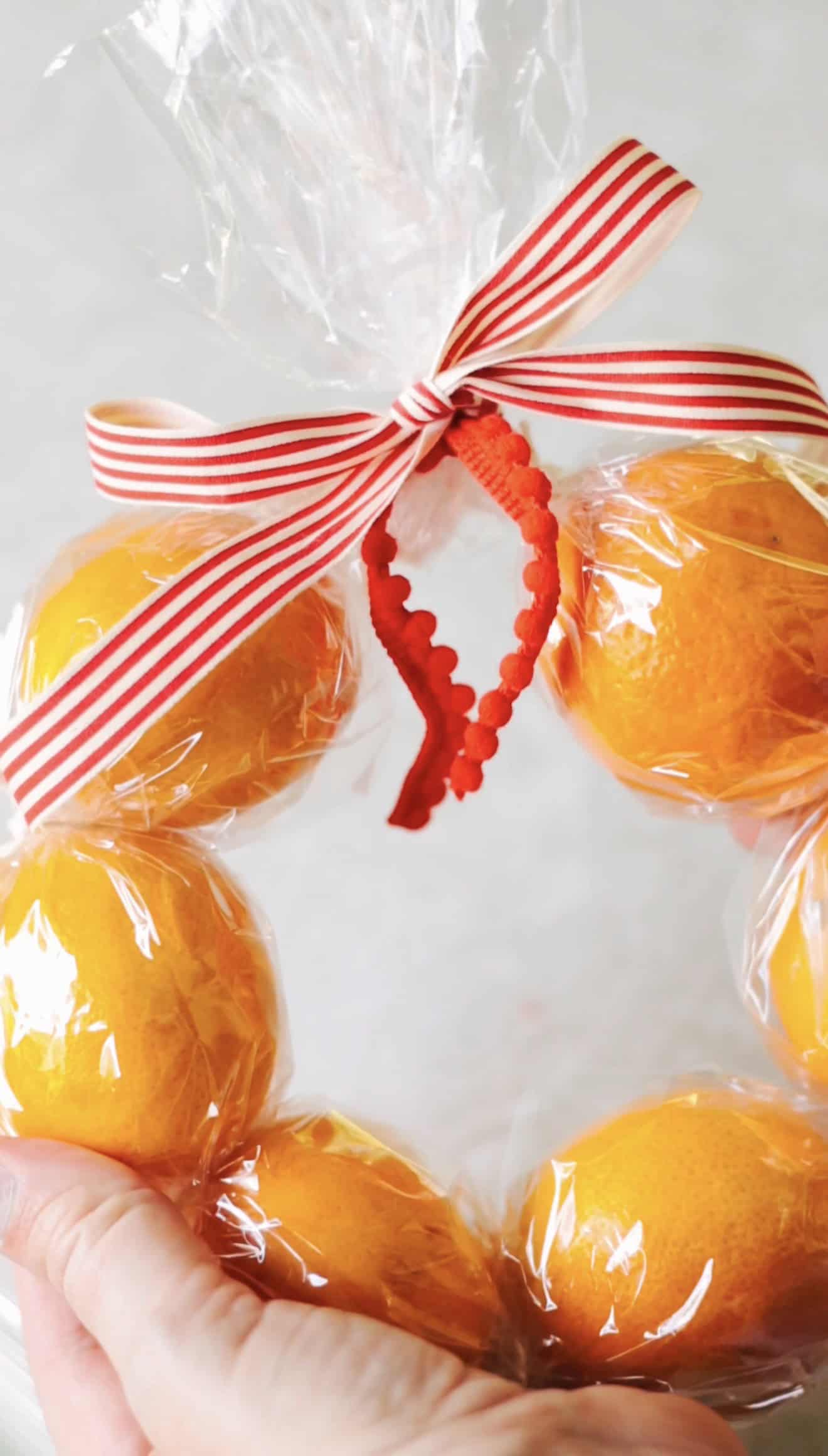 Hands holding clementine wreath with red and white bow.