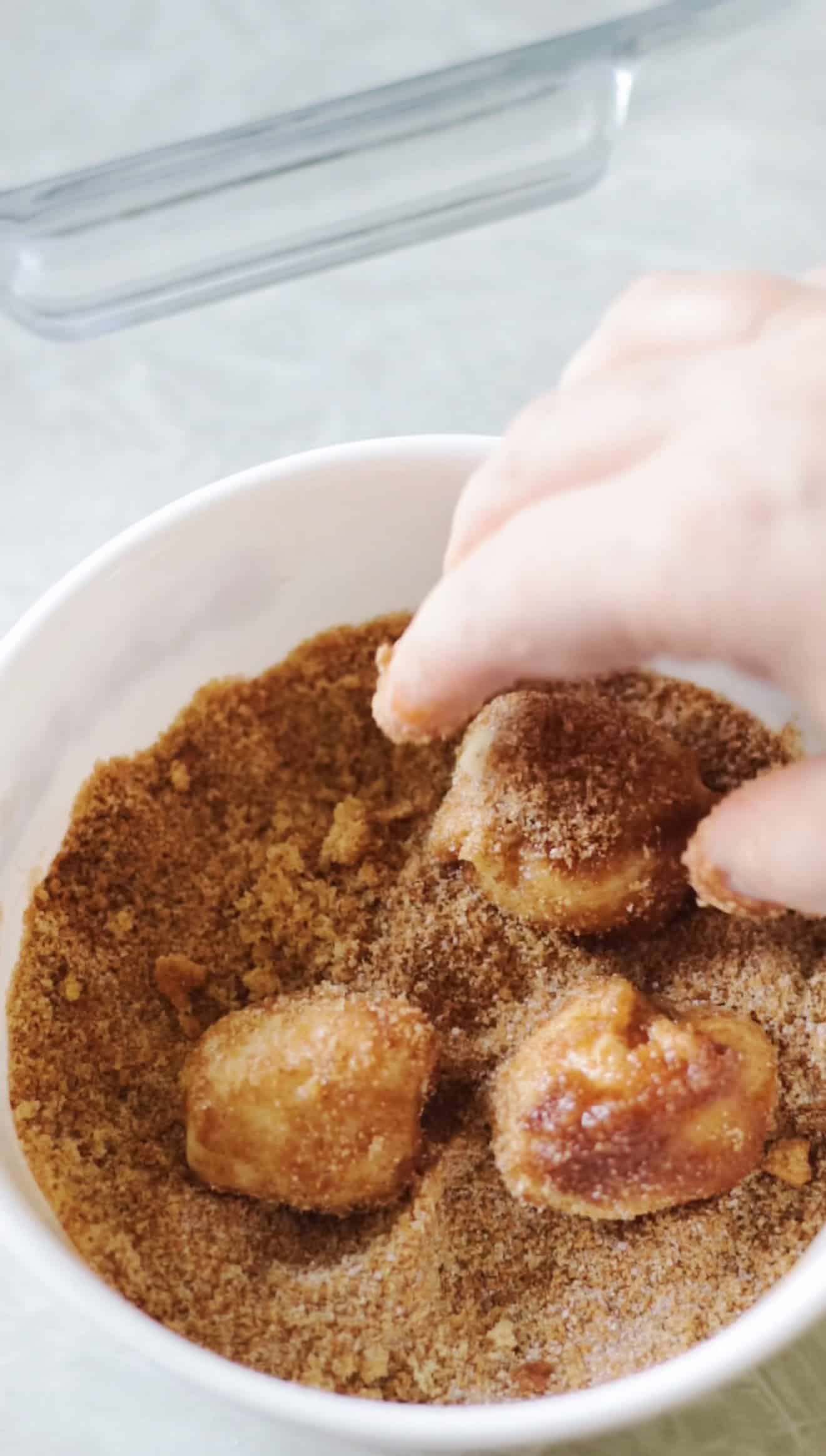 Hand rolling balls of dough in a bowl of cinnamon and sugar.