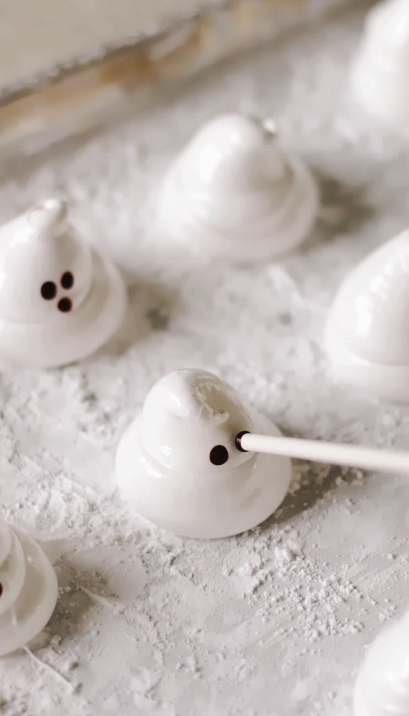 Eyes being added to marshmallows using a lollipop stick dipped in baking cocoa and water.