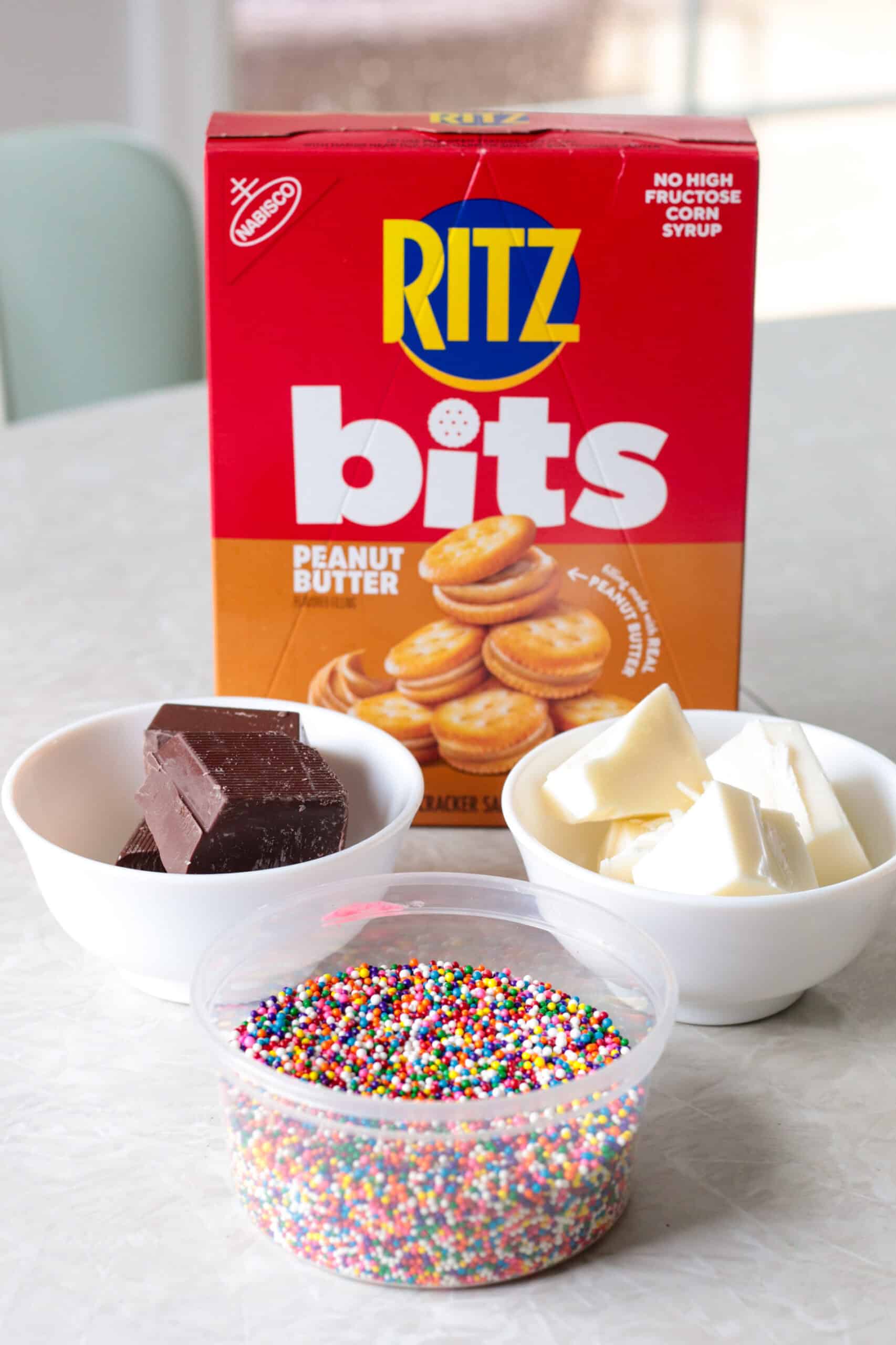 Box of peanut butter crackers, almond bark and container of non pareils sprinkles.