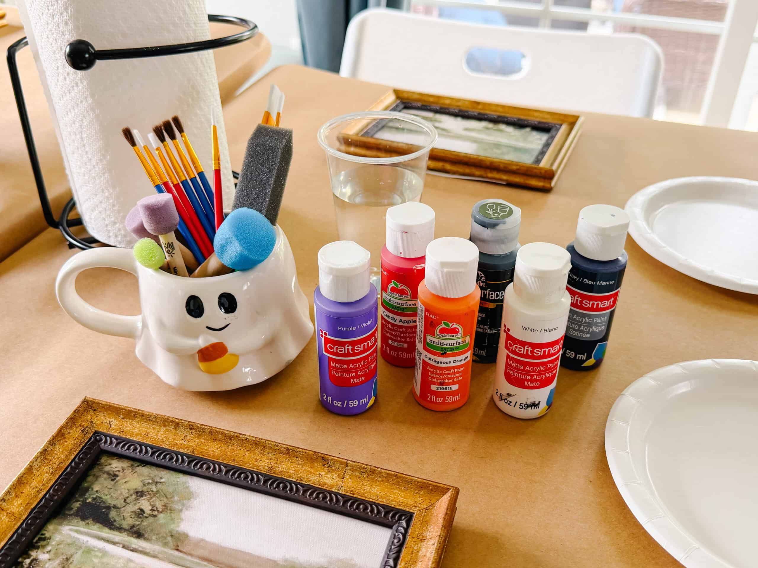Bottles of acrylic paint, ghost mug with paint brushes.