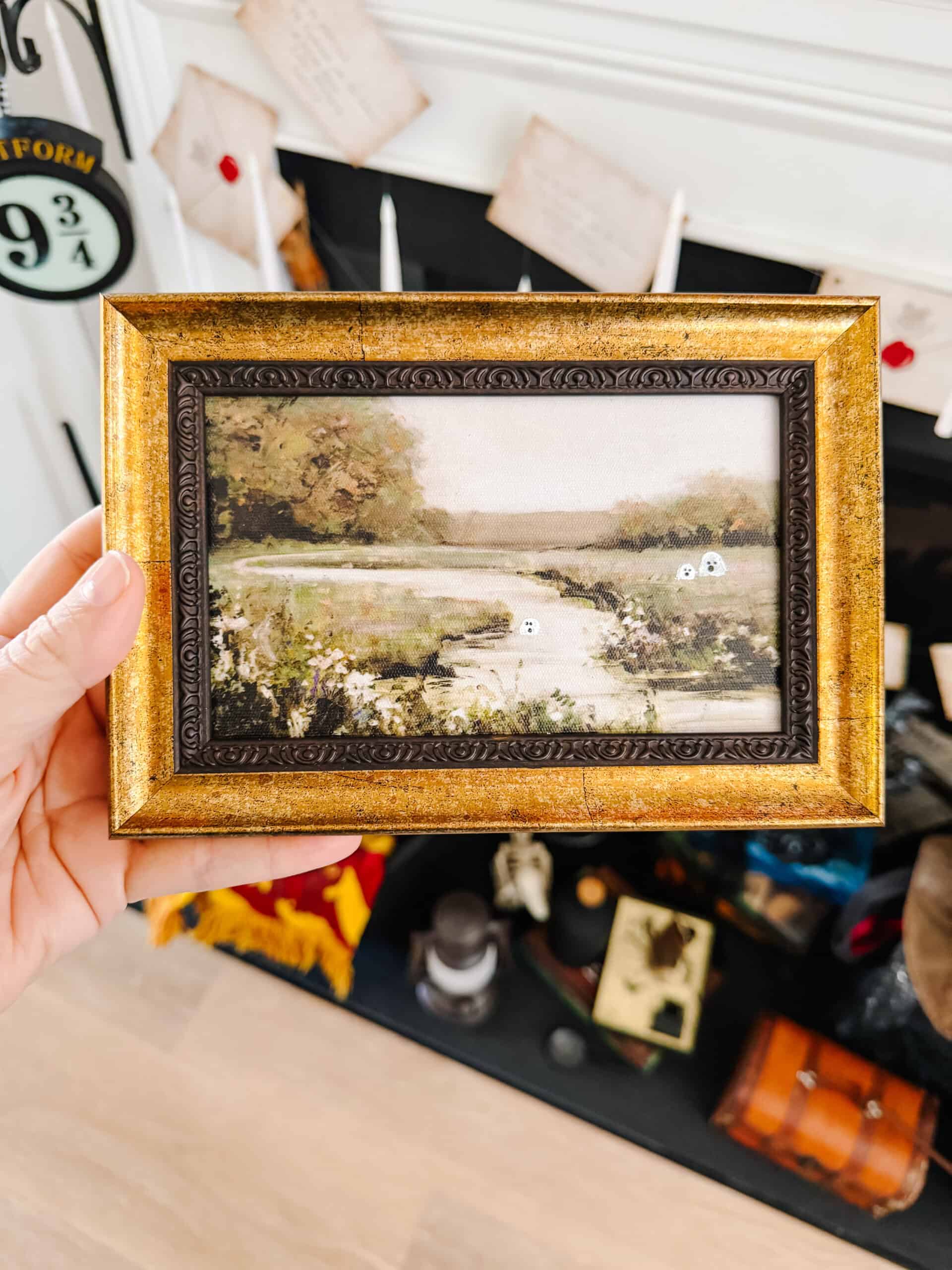 Framed landscape painting with miniature ghosts painted on top.