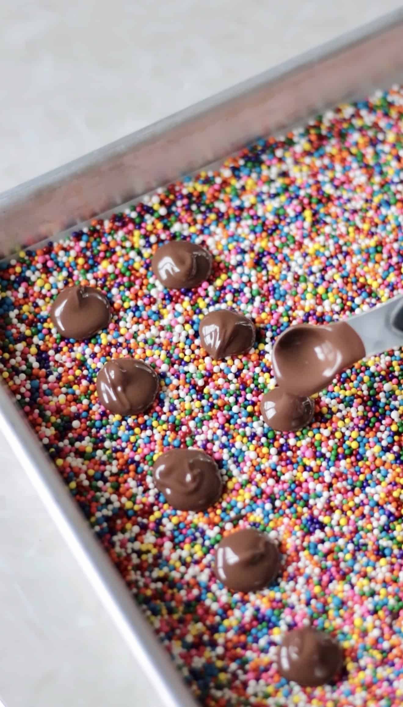 Spoonfulls of chocolate added to tray of sprinkles.