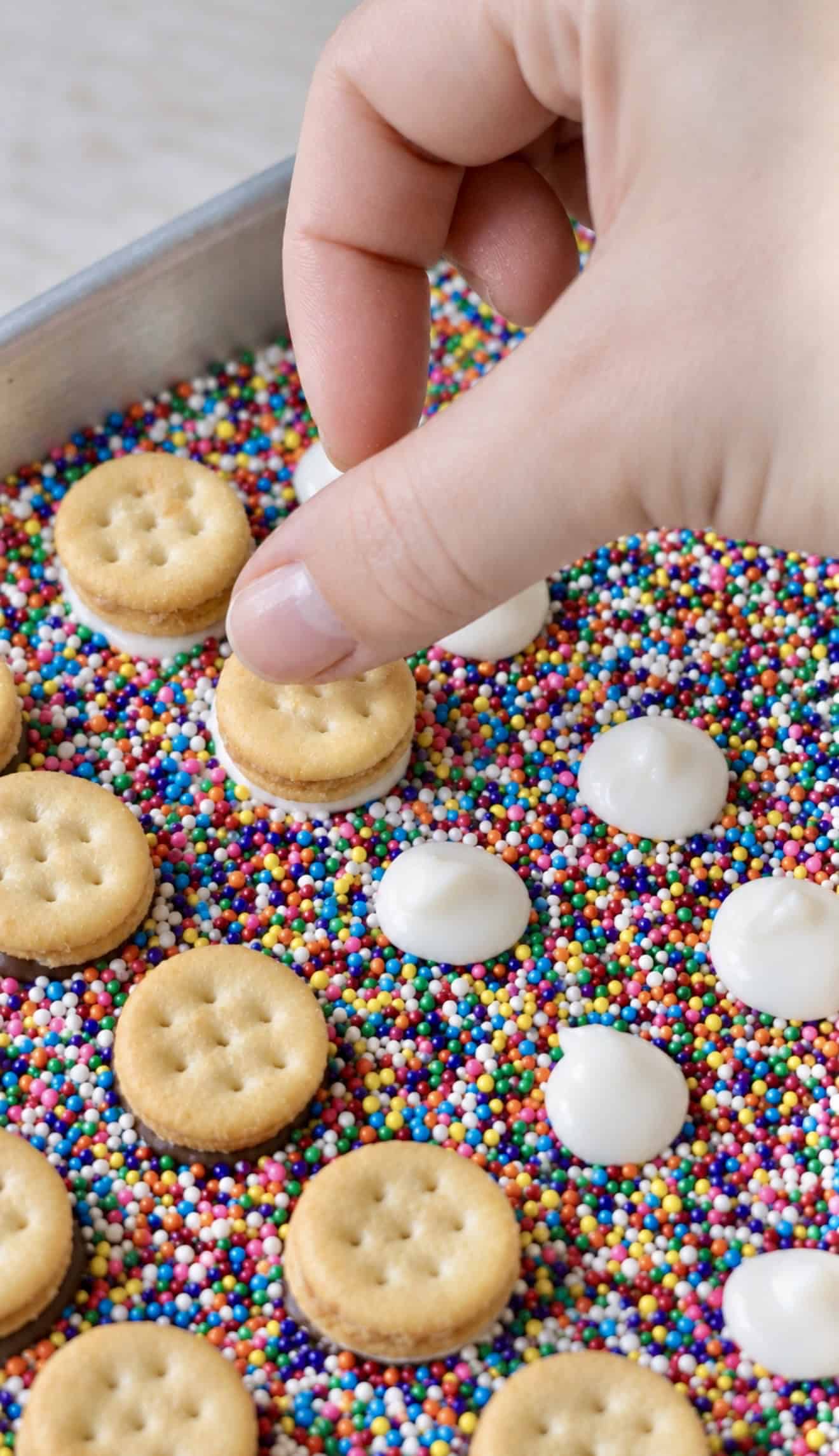 Hand adding crackers to the tops of drops of melted chocolate.