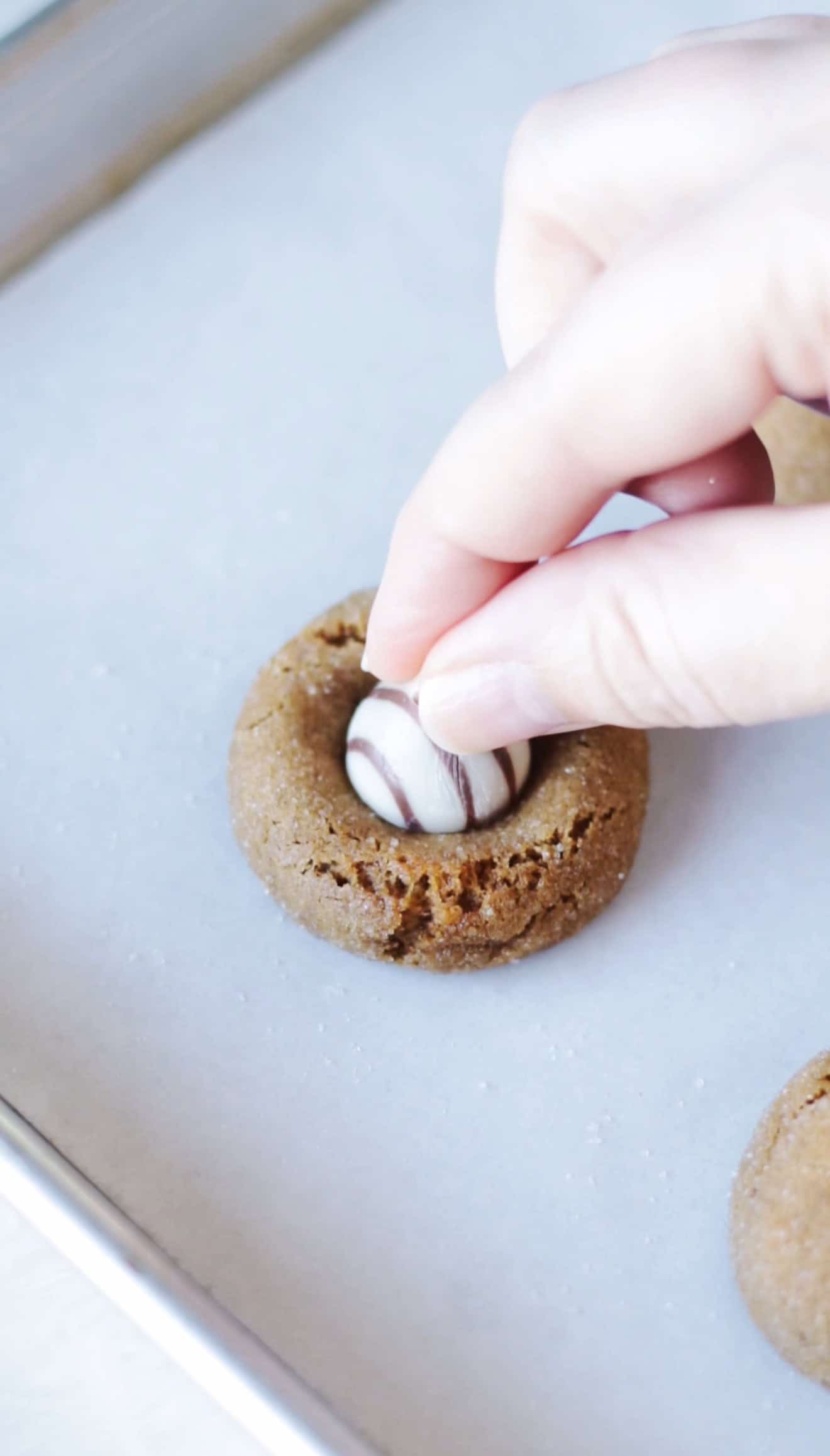 Hand pressing hershey kiss into warm cookie.